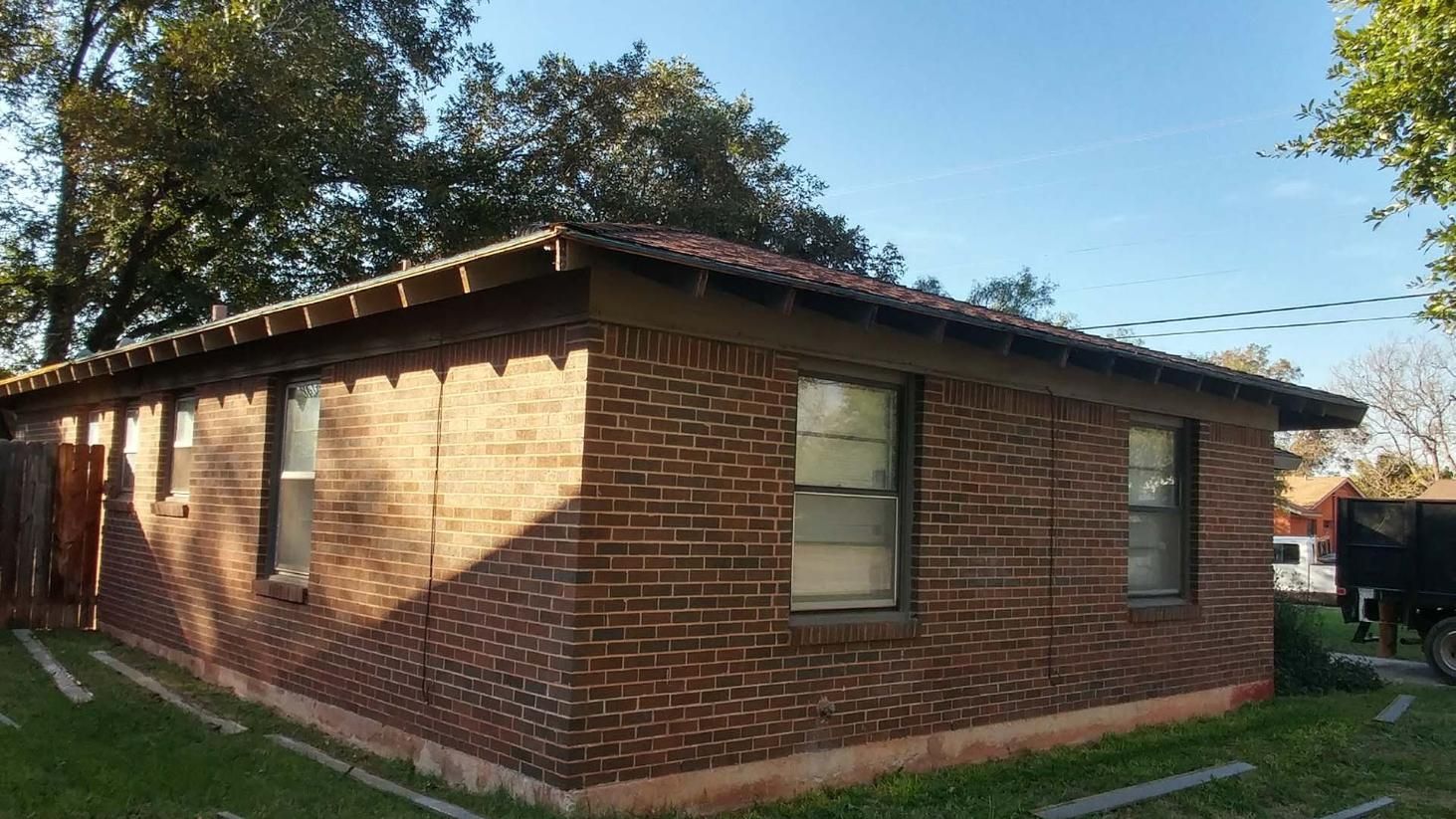 Single-story brick house with a low roof and small windows in a sunny yard.