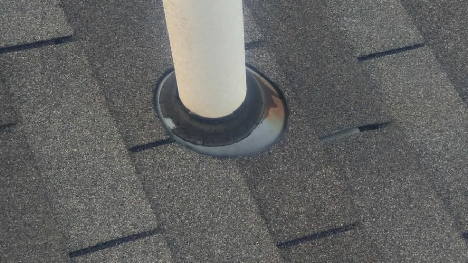 White vent pipe with black flashing on a gray shingle roof.