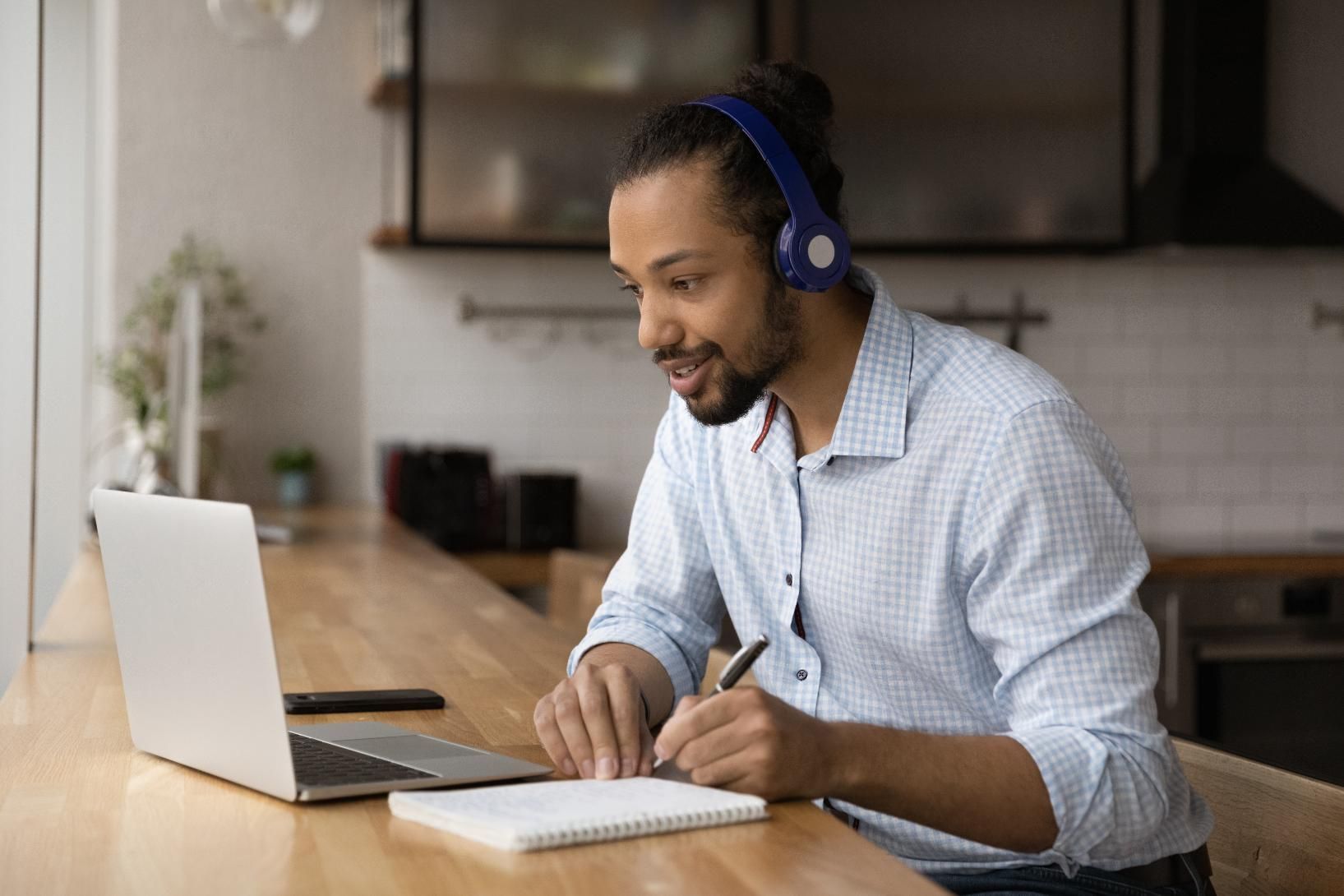 Man wearing headphones typing at a laptop in a kitchen workspace