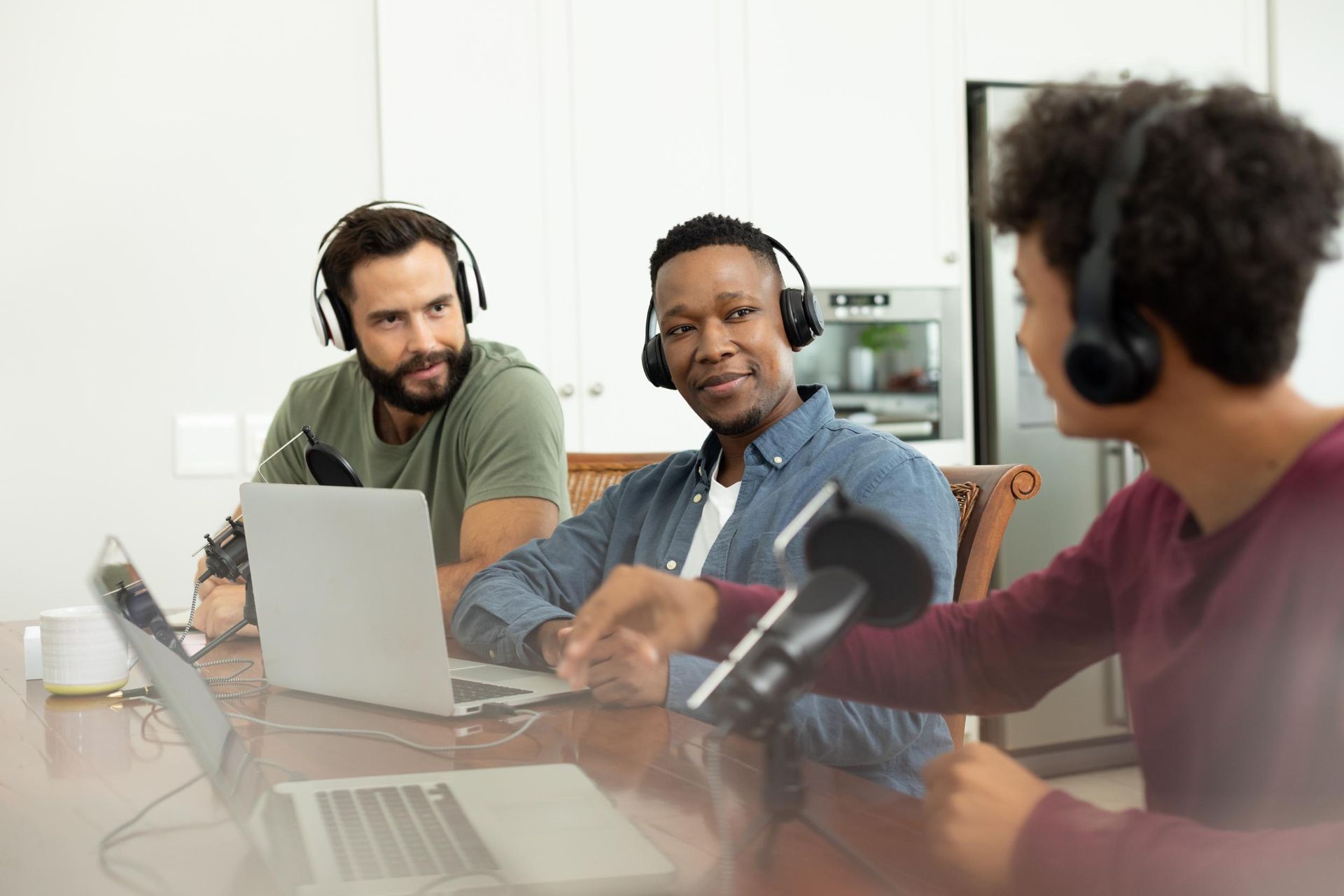 Three people in a meeting room wearing headsets, talking around a laptop and glass table.