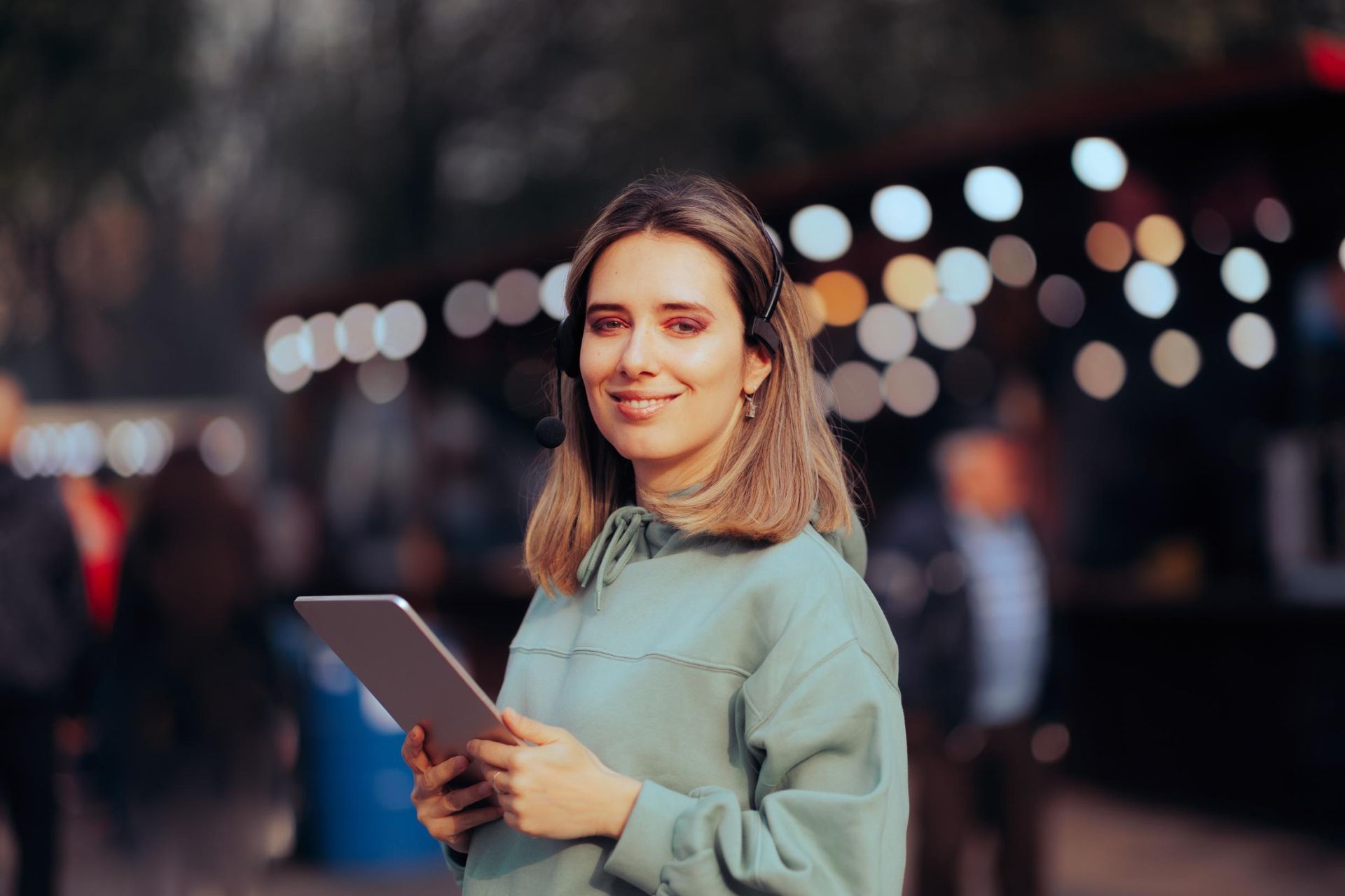 Woman holding a tablet at an outdoor event with blurred lights in the background