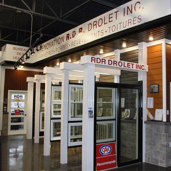 Intérieur d'une entreprise de rénovation, présentant portes et fenêtres. L'enseigne indique le nom de l'entreprise et ses services.