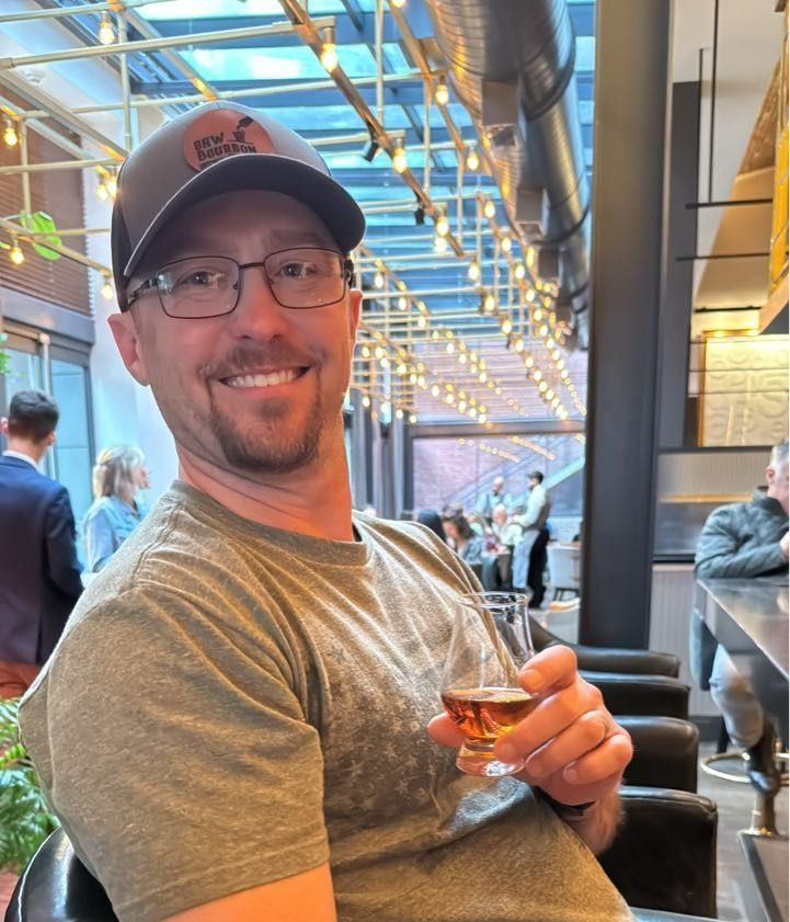 Smiling man in a cap holding a drink at a modern indoor bar or lounge