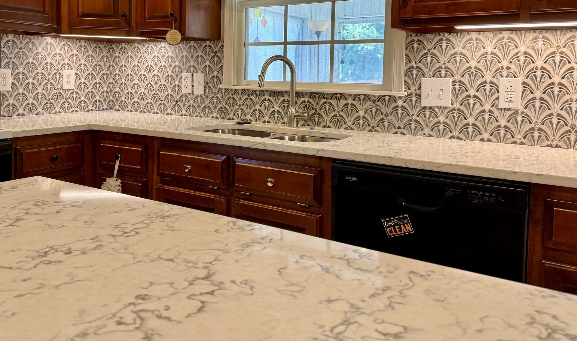 Modern kitchen with marble countertops, patterned tile backsplash, wooden cabinets, and a window above the sink
