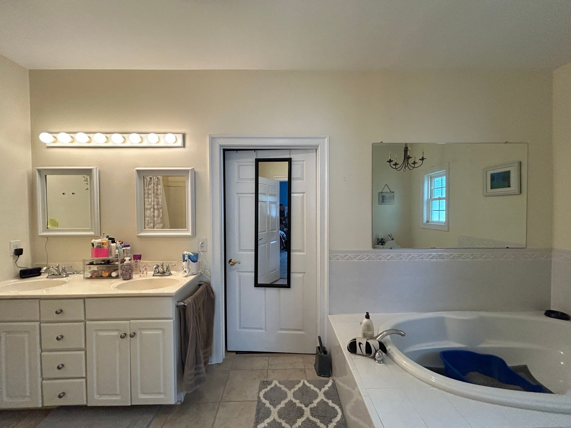 Bathroom with white vanity, large mirror, glass shower door, and a built-in tub with a blue cover.