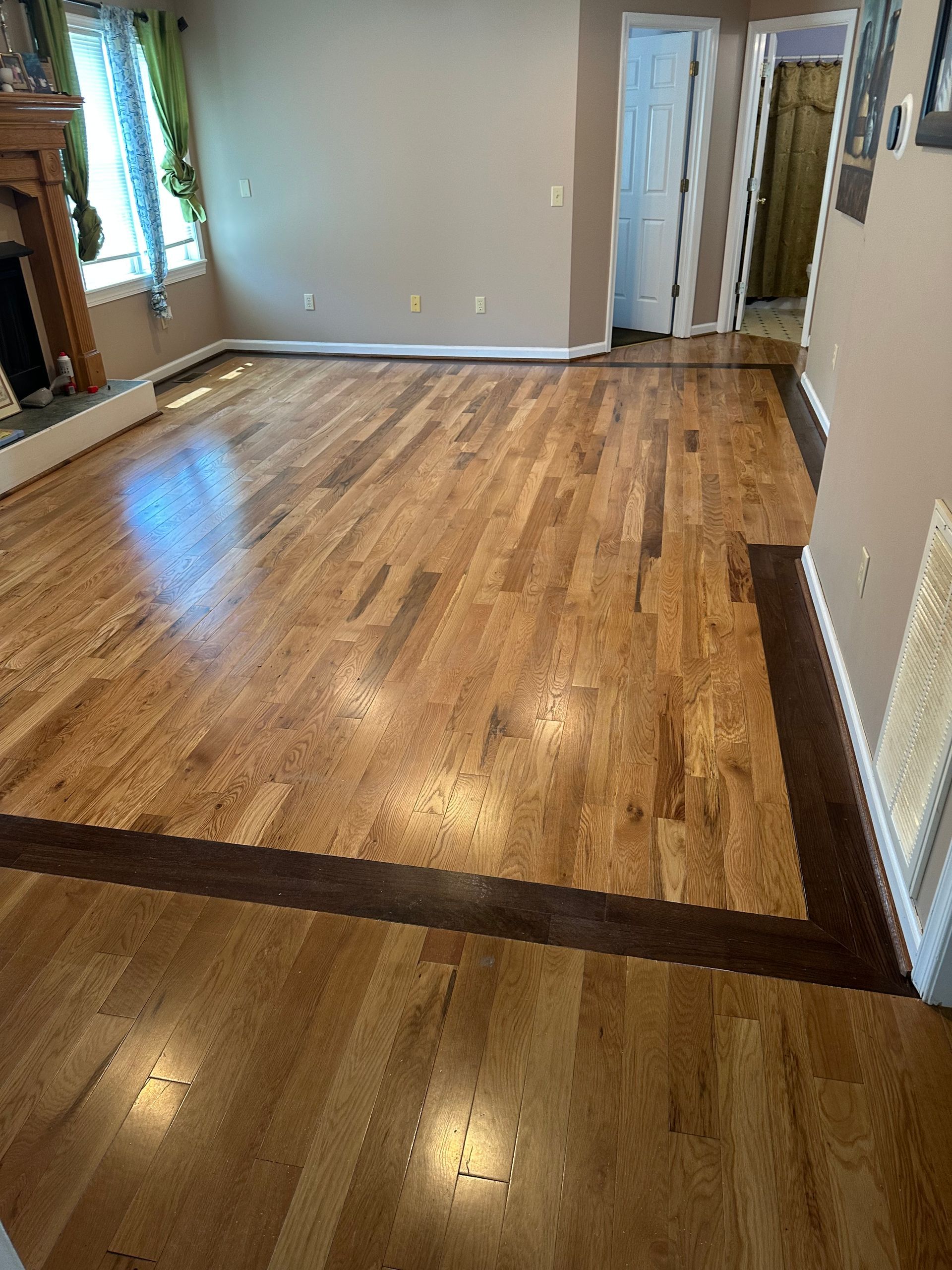 Empty living room with hardwood floors, light gray walls, and a hallway opening on the right