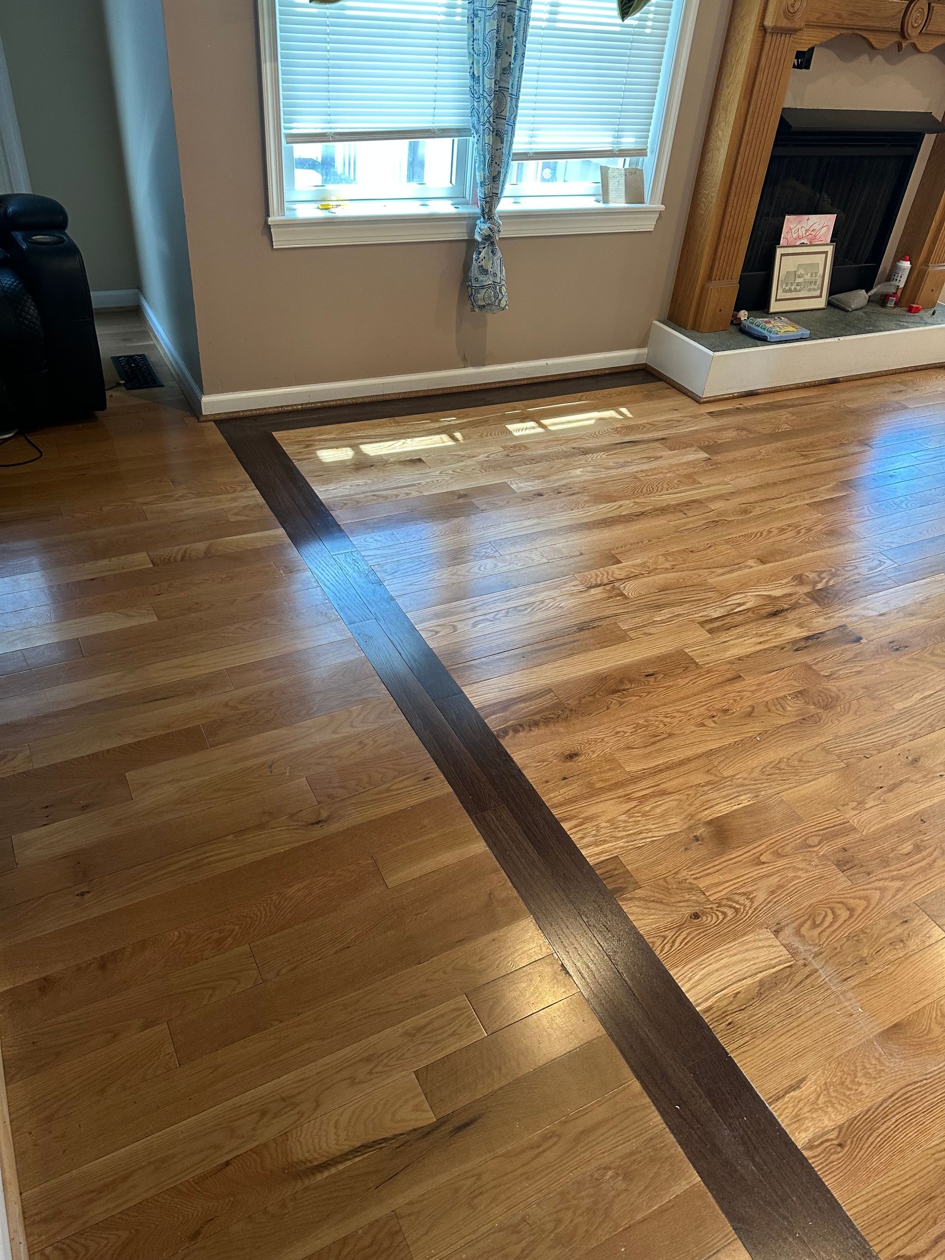 Living room with hardwood floor, window, and fireplace, showing a dark line across the floor