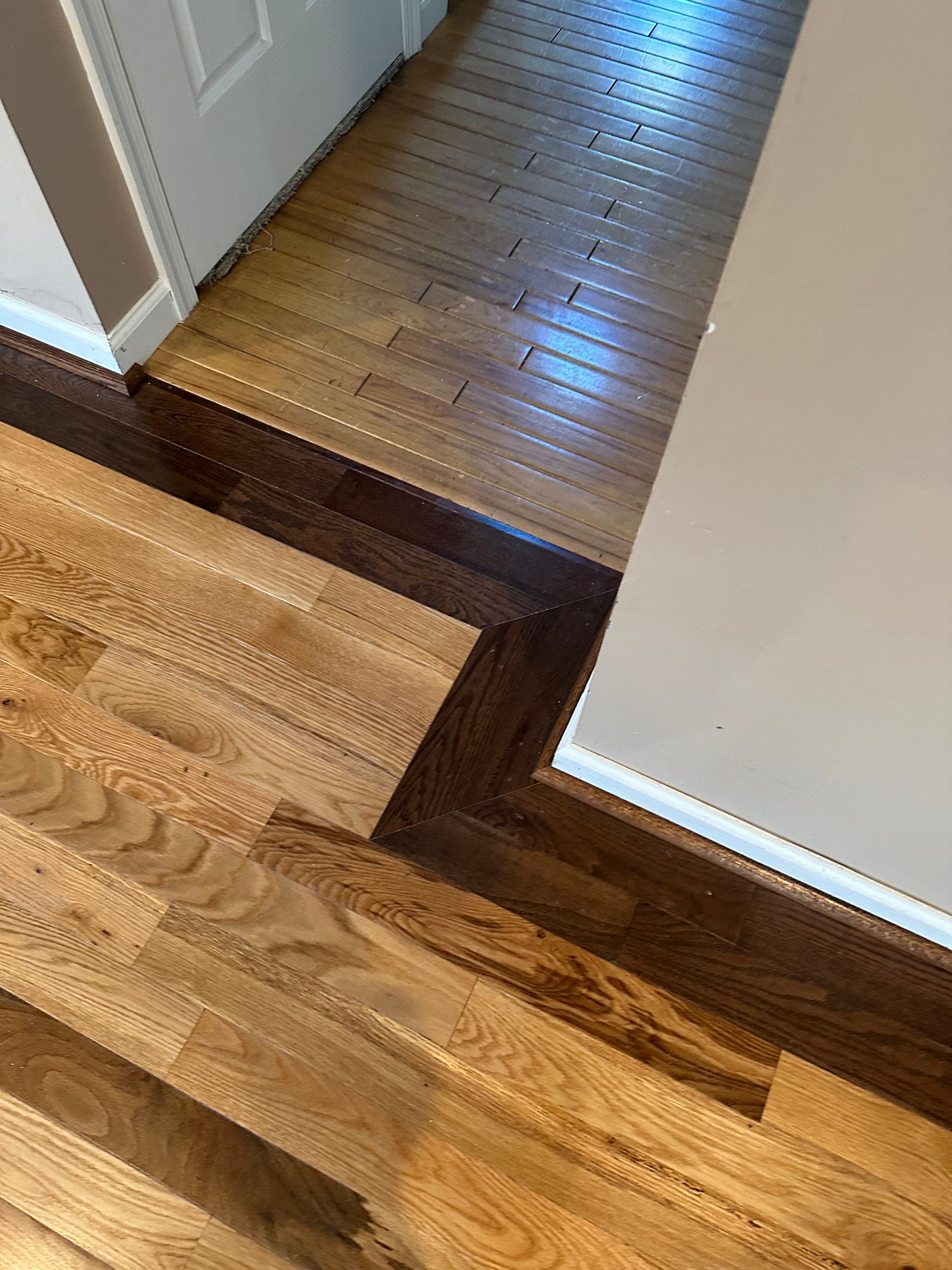 Wood floor meeting a dark threshold strip between two hallways with white walls and door frames