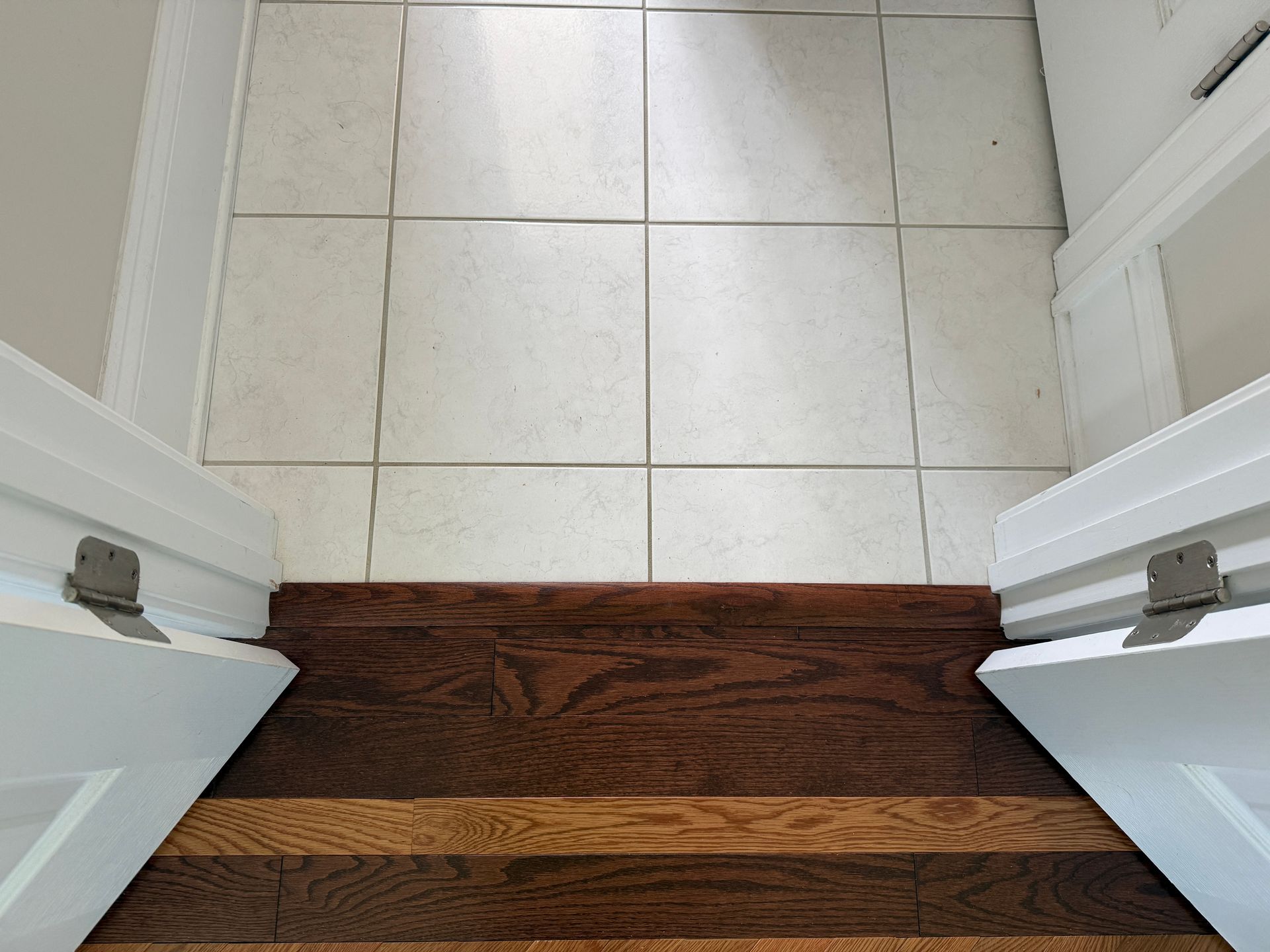 Open doorway with white tile floor and dark wood threshold, seen from above.