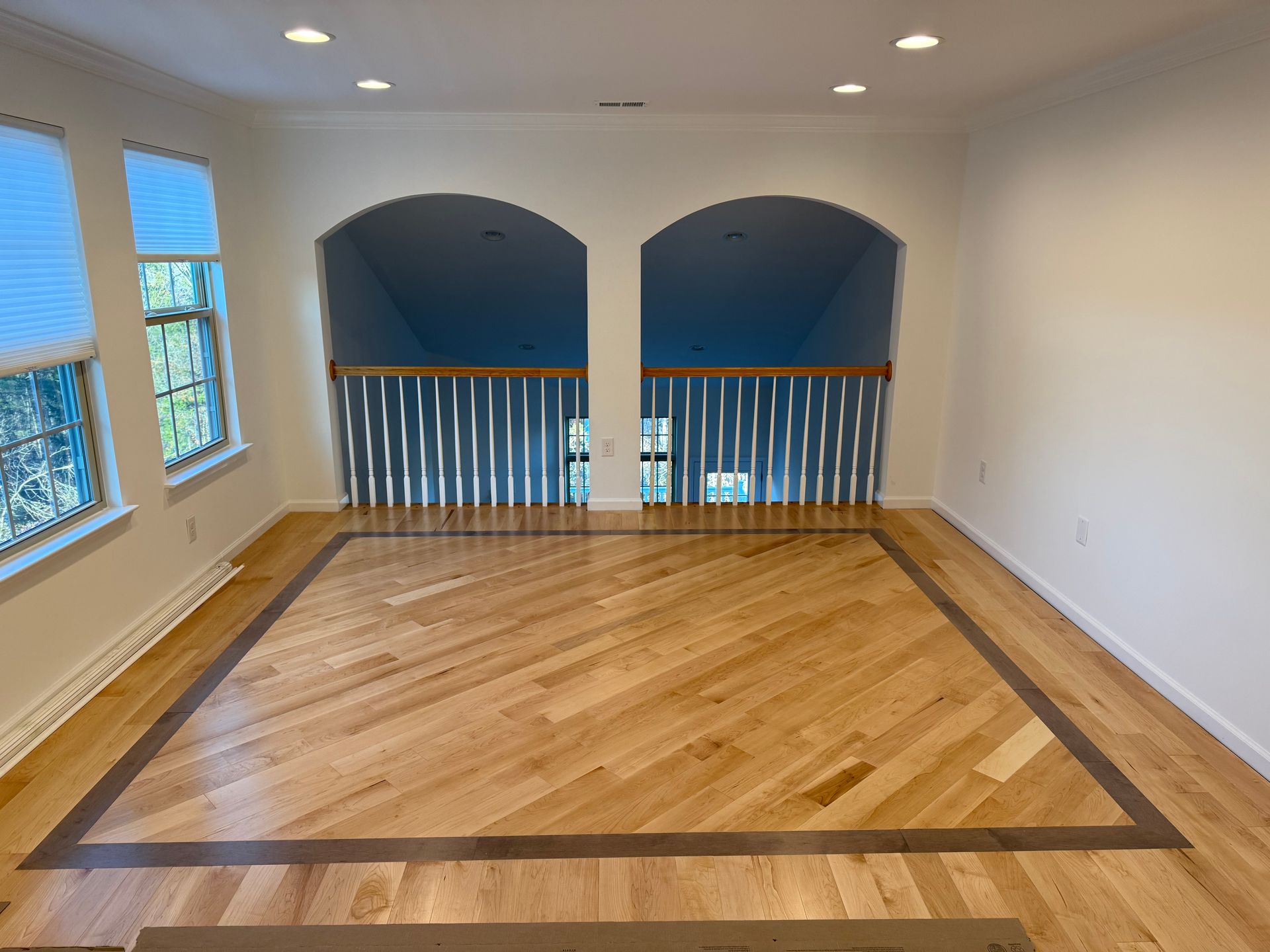 Empty upstairs room with hardwood floor, arched openings, and blue walls overlooking a railing and windows