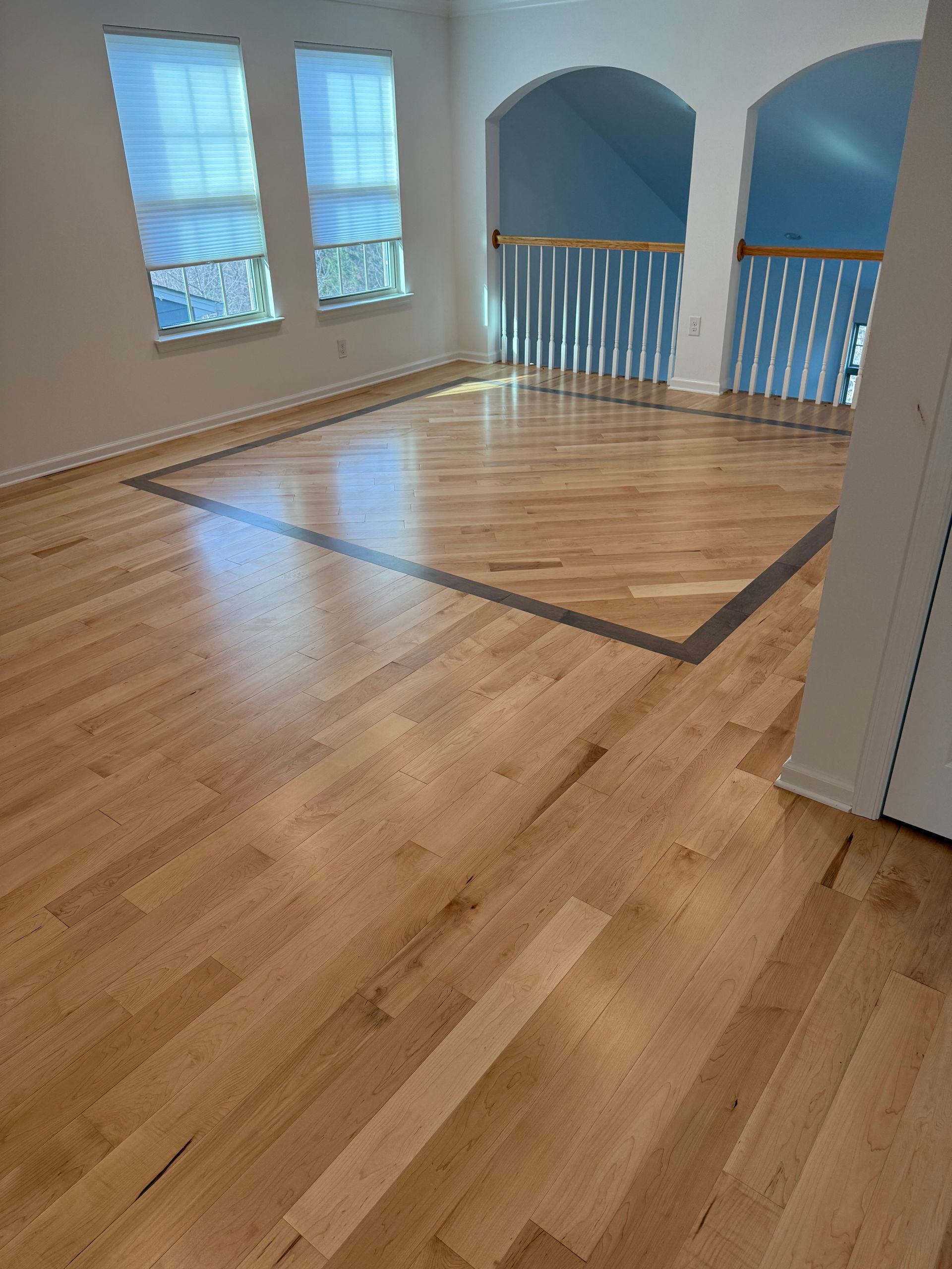Empty hardwood room with windows and blue railings overlooking a stairwell