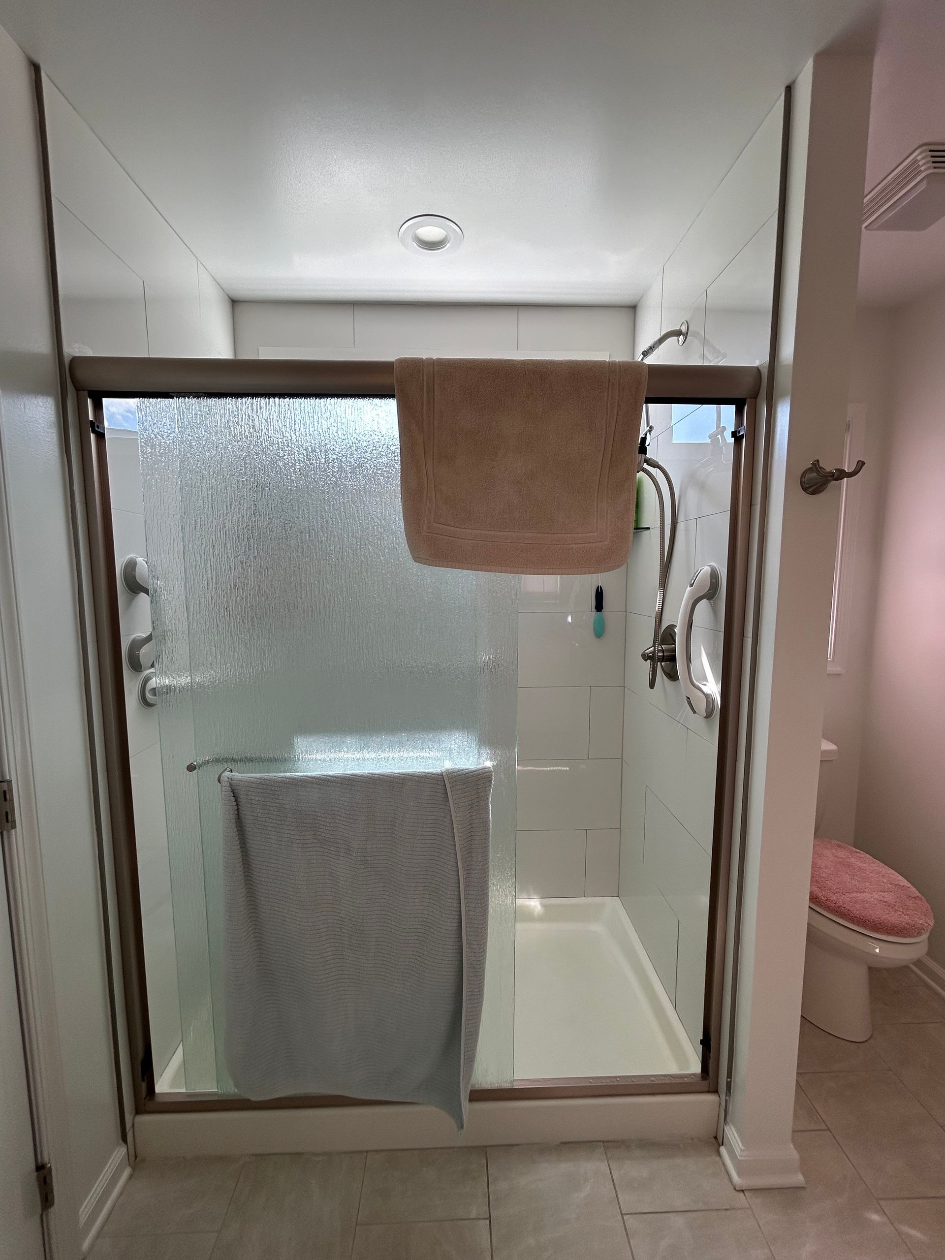 Small bathroom with frosted glass shower doors and towels hanging inside the doorway.