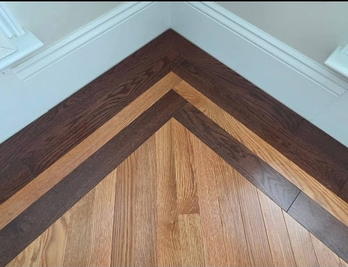 Wood floor corner with dark and light herringbone wood trim against white baseboards