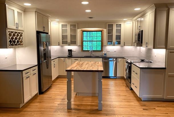 A kitchen with white cabinets , black counter tops , stainless steel appliances and a wooden island.