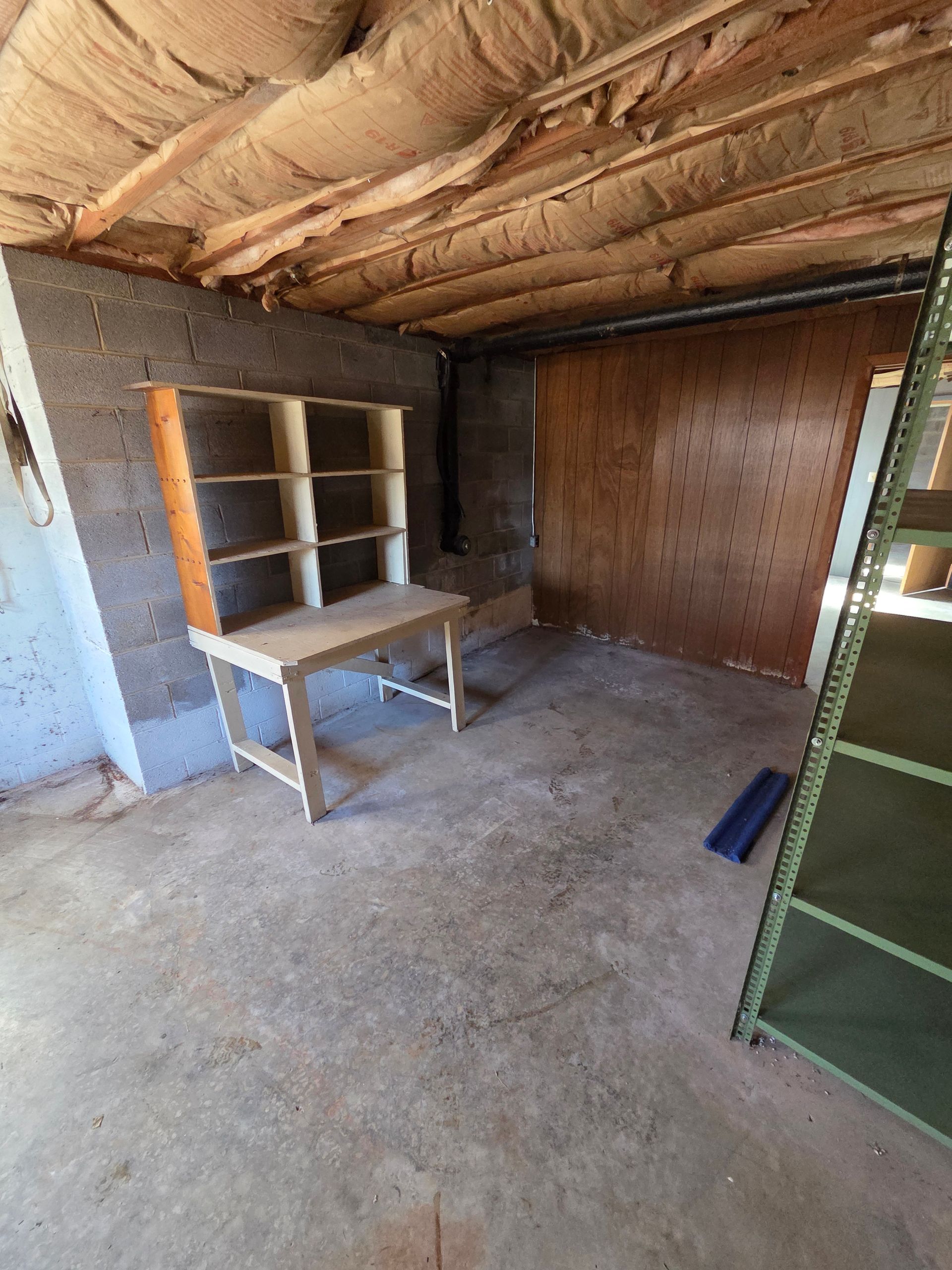 Empty storage room with concrete floor, exposed insulated ceiling, and metal shelving units.