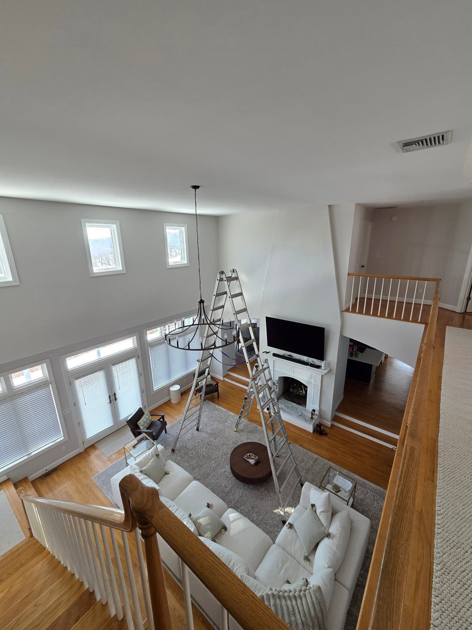 Bright living room with white sofas, a ladder, TV, and a loft railing overlooking windows and stairs