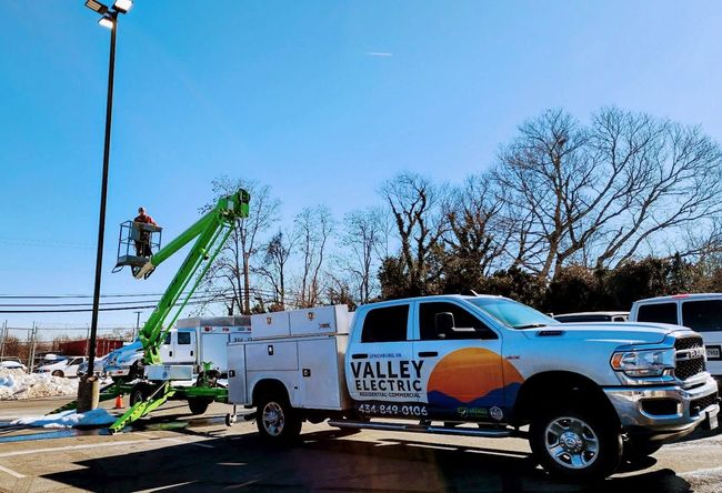 Utility truck and green lift bucket beside a snowy roadside with workers trimming trees