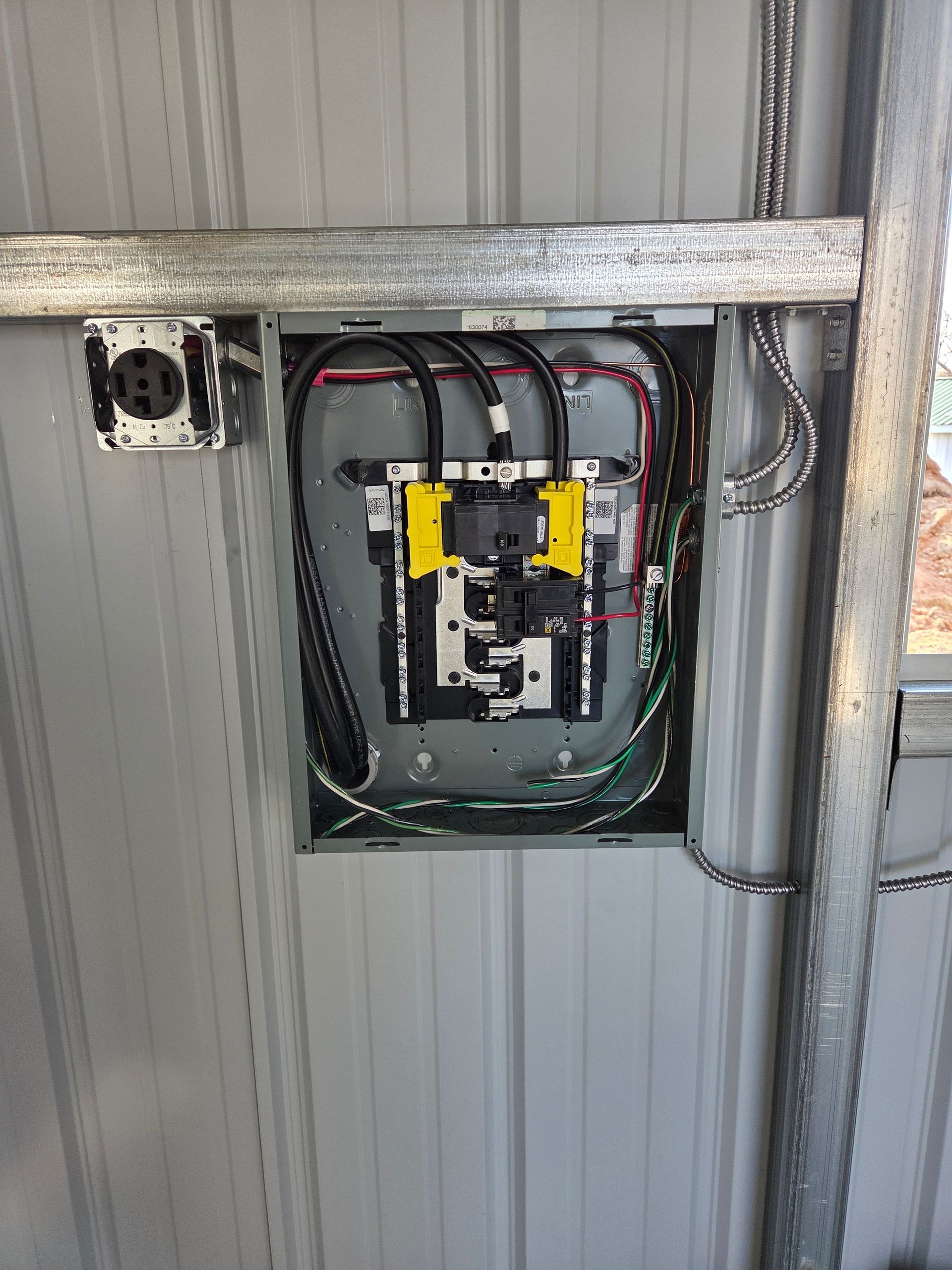 Open electrical panel with wires mounted on a corrugated metal wall.