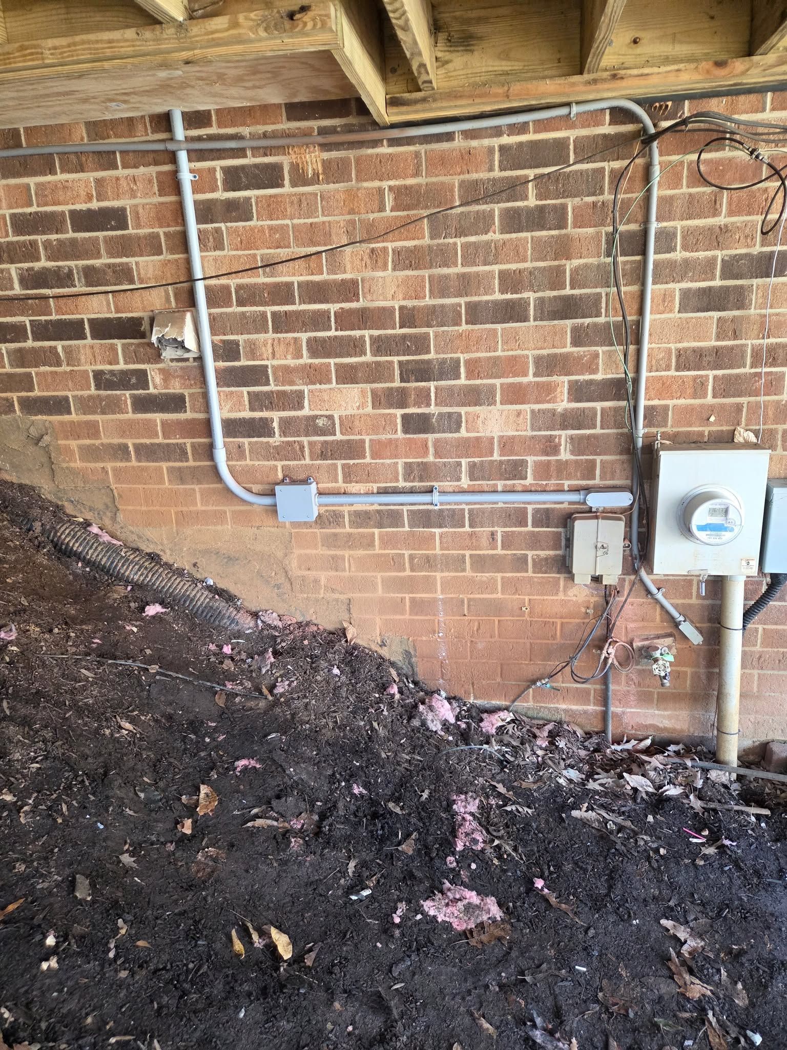 Brick basement wall with exposed conduit and an electrical box beside a dark soil pile