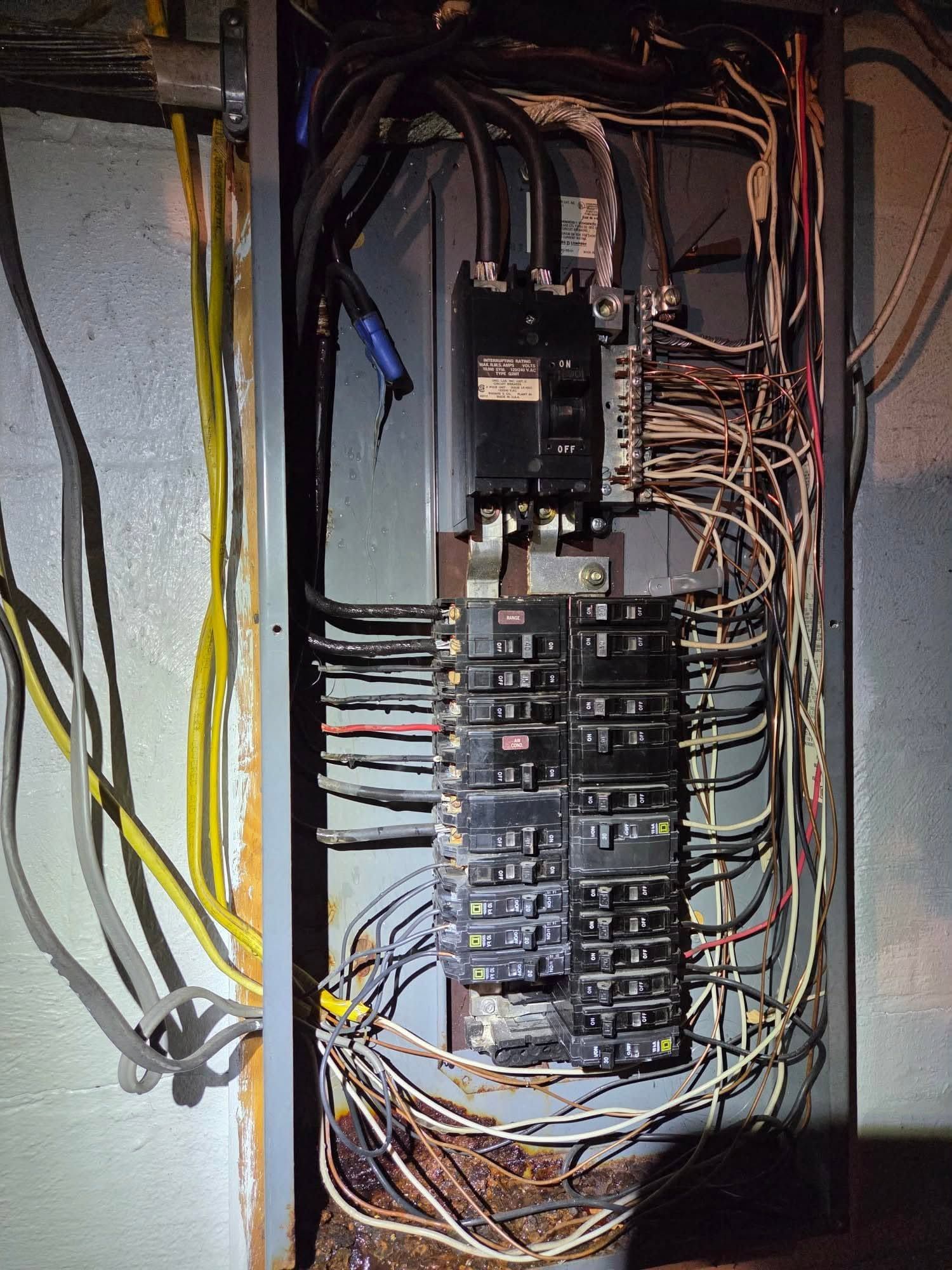 Open electrical breaker panel with tangled wires and multiple circuit breakers on a wall
