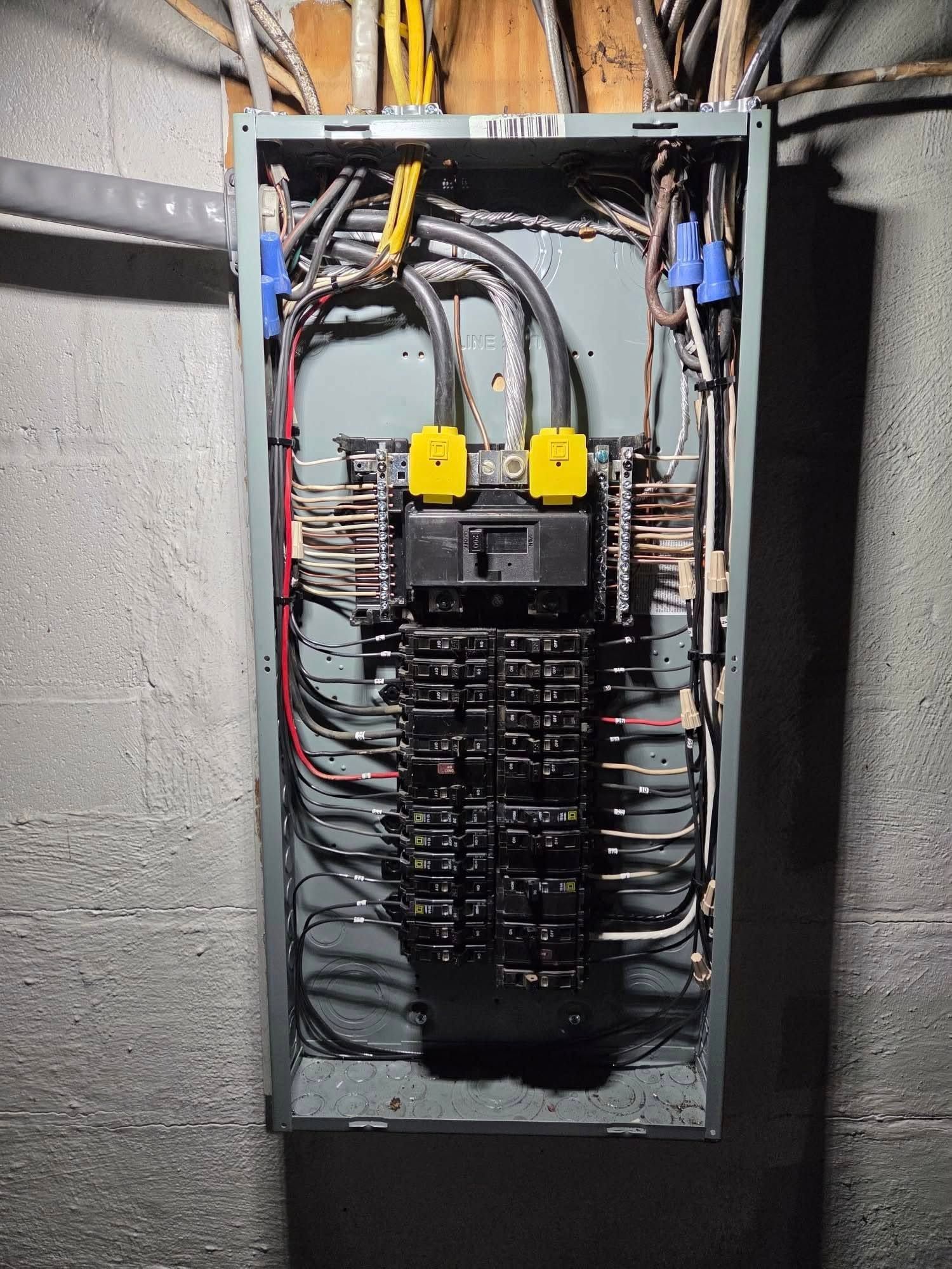 Electrical breaker panel with yellow handles and bundled wires in a gray utility room