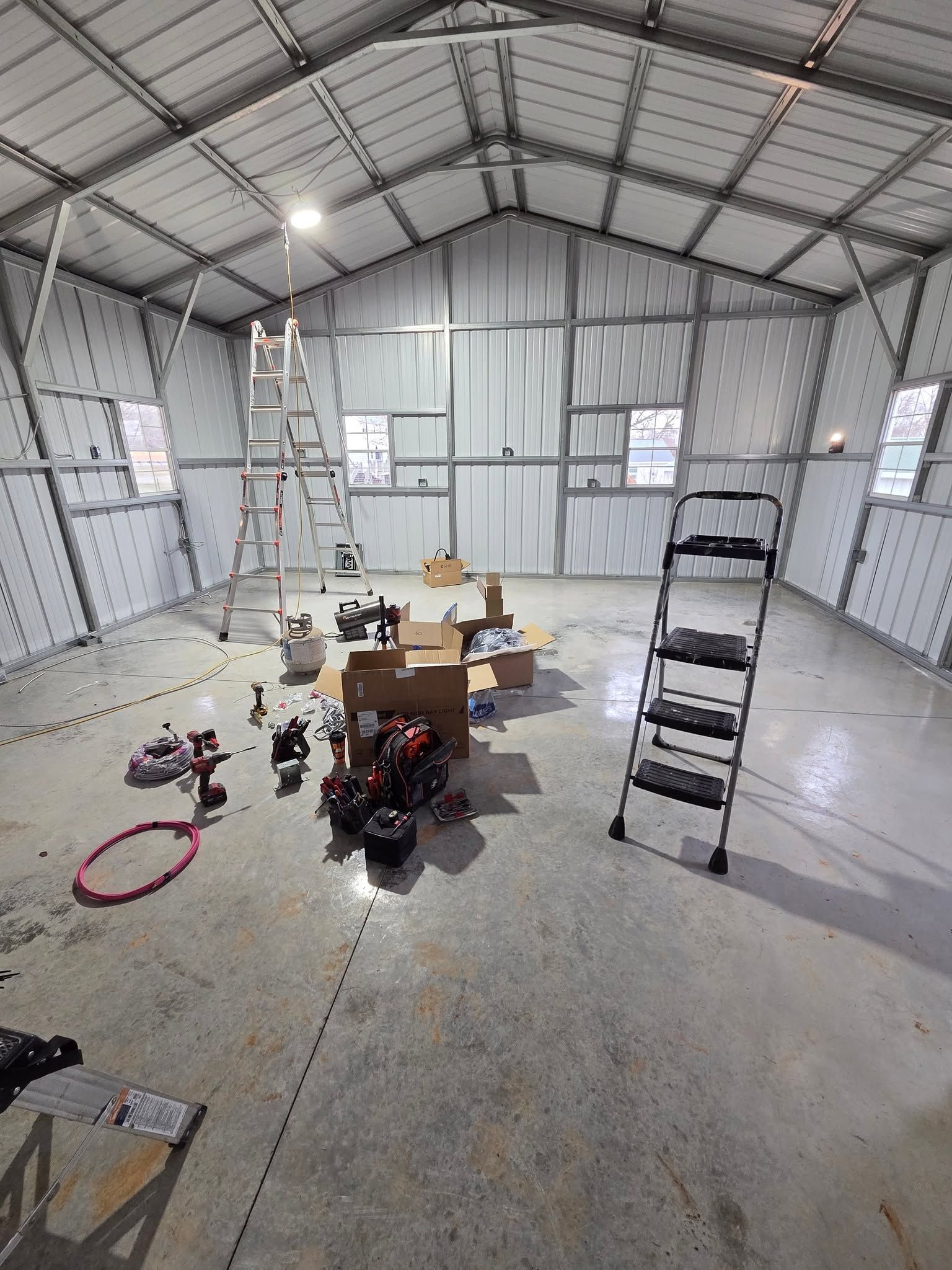 Empty metal workshop with ladder, tools, and boxes on a concrete floor