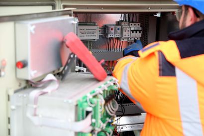Technician in orange safety vest working inside an electrical control panel cabinet