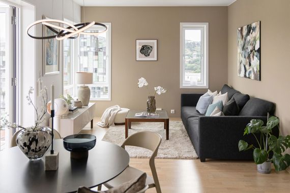 Modern living room with dark gray sofa, round black table, plants, and large windows with city view
