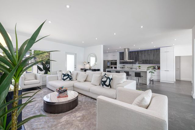Modern open-plan living room with white sofas, gray rug, and kitchen in the background
