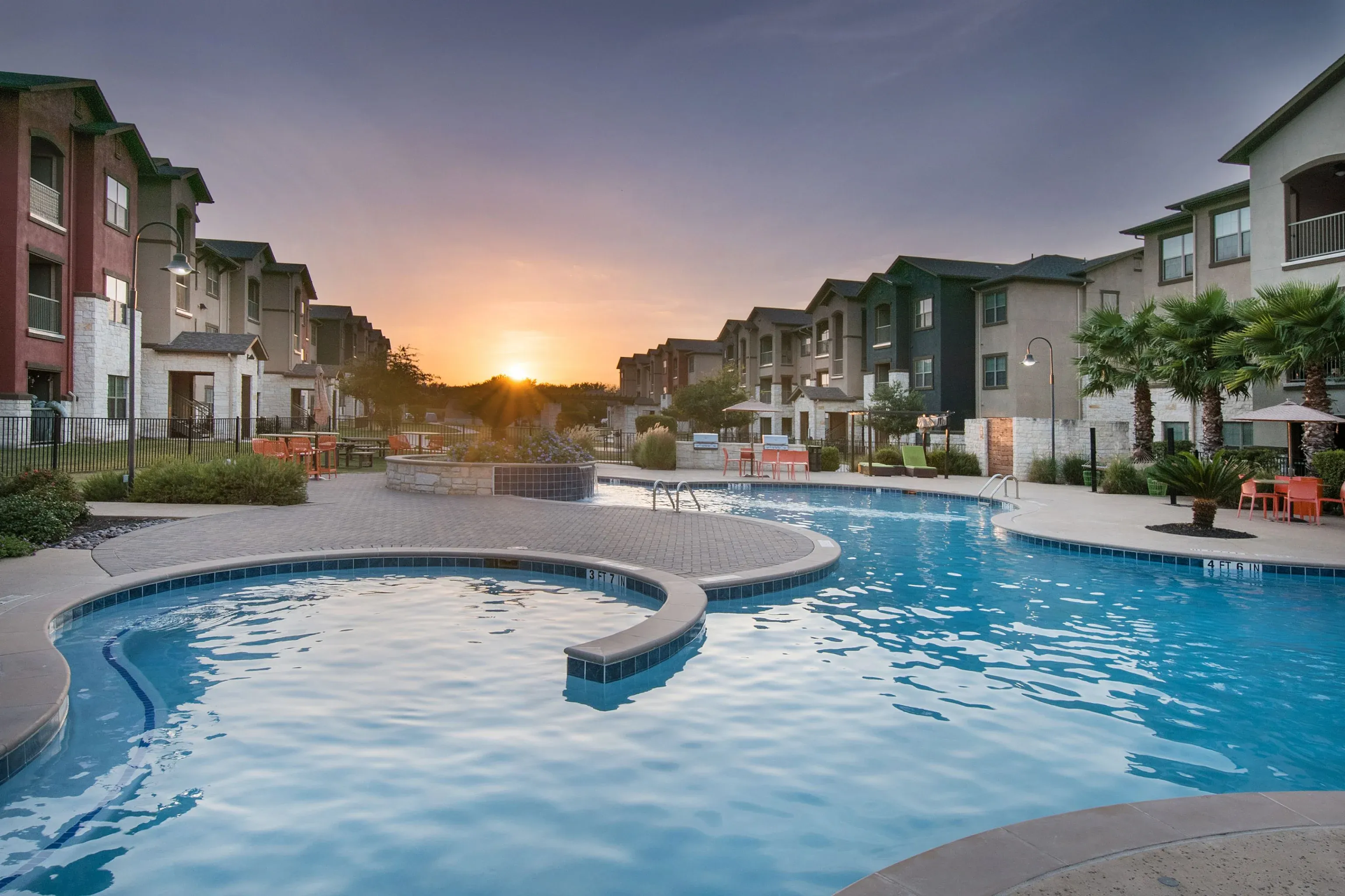 Sunset-view outdoor pool surrounded by seating and apartment buildings.