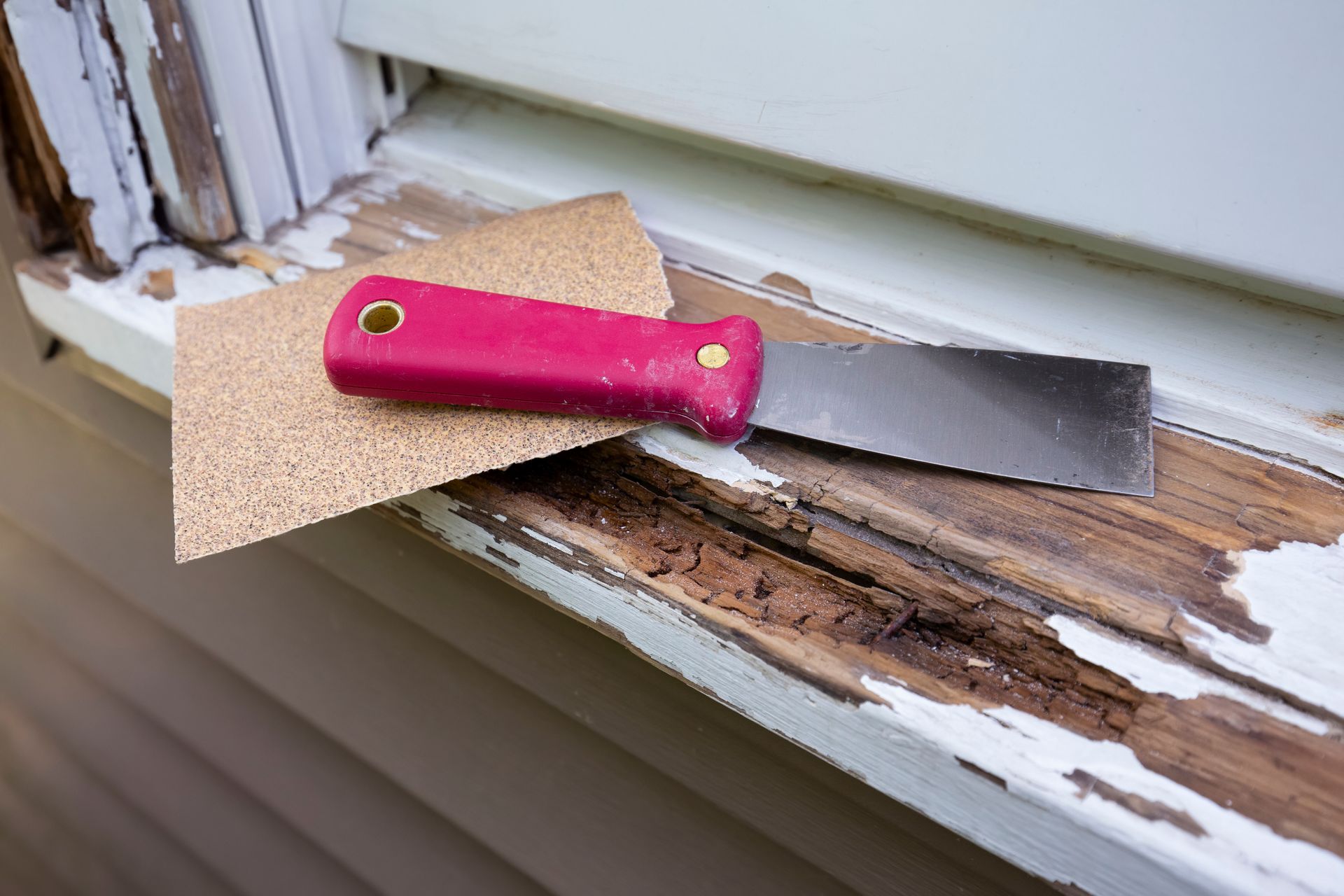 A spatula and sandpaper are sitting on a window sill.