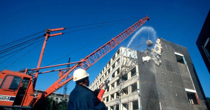 Construction worker watching a building demolition with cranes against a blue sky