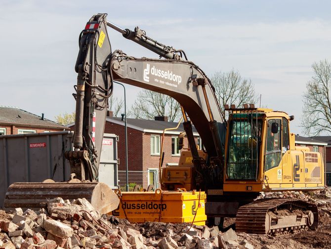 Yellow excavator at a demolition site beside debris and houses