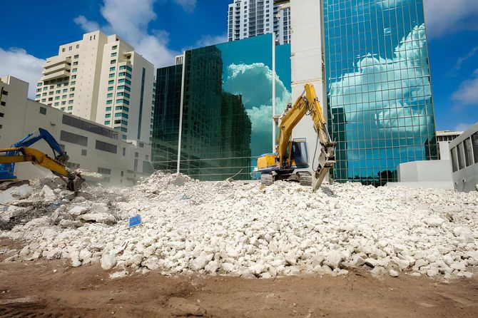 Demolition site with excavators clearing rubble in front of modern glass high-rises