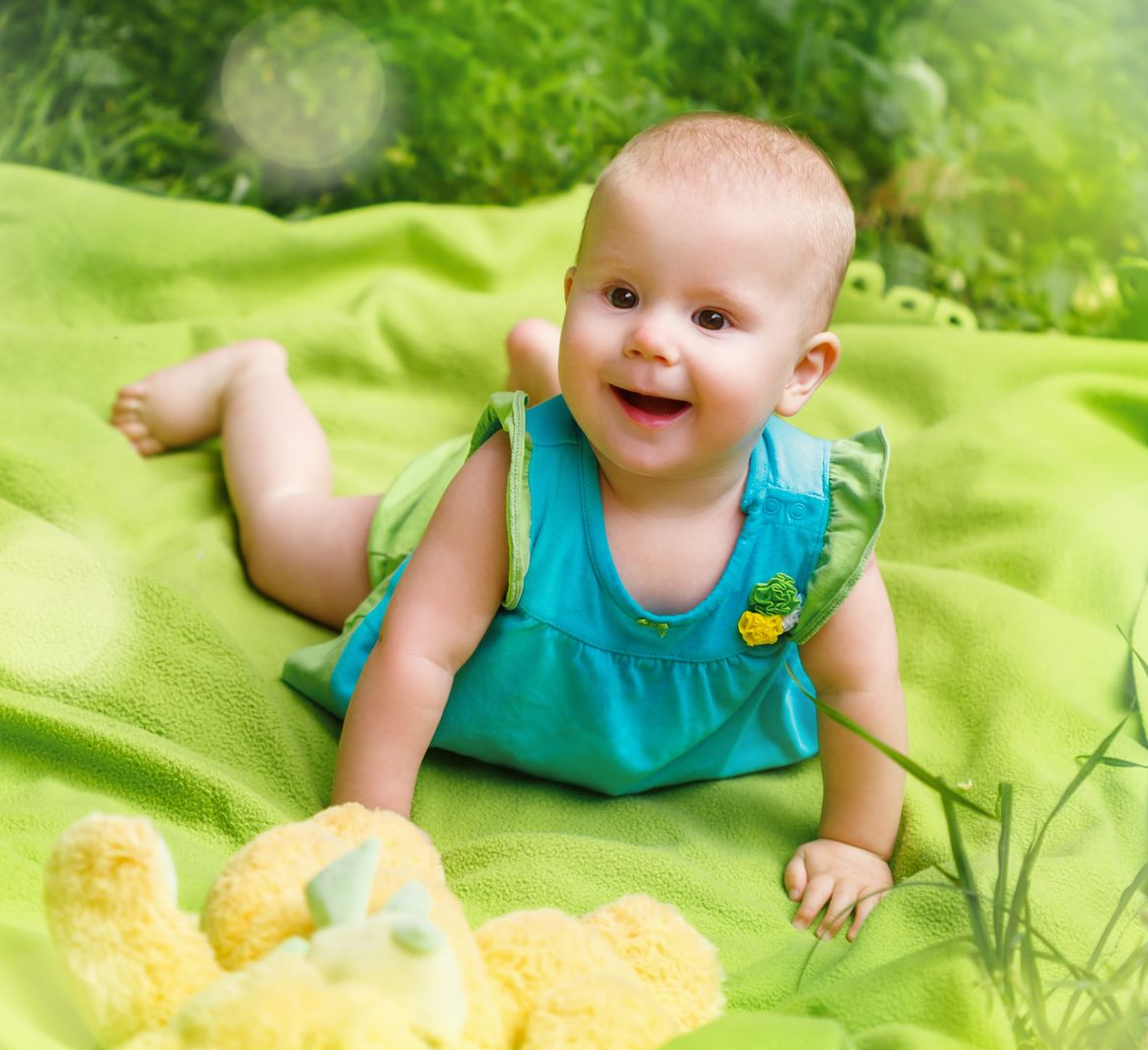 Young baby laying on its stomach on a green blanket in  the park.