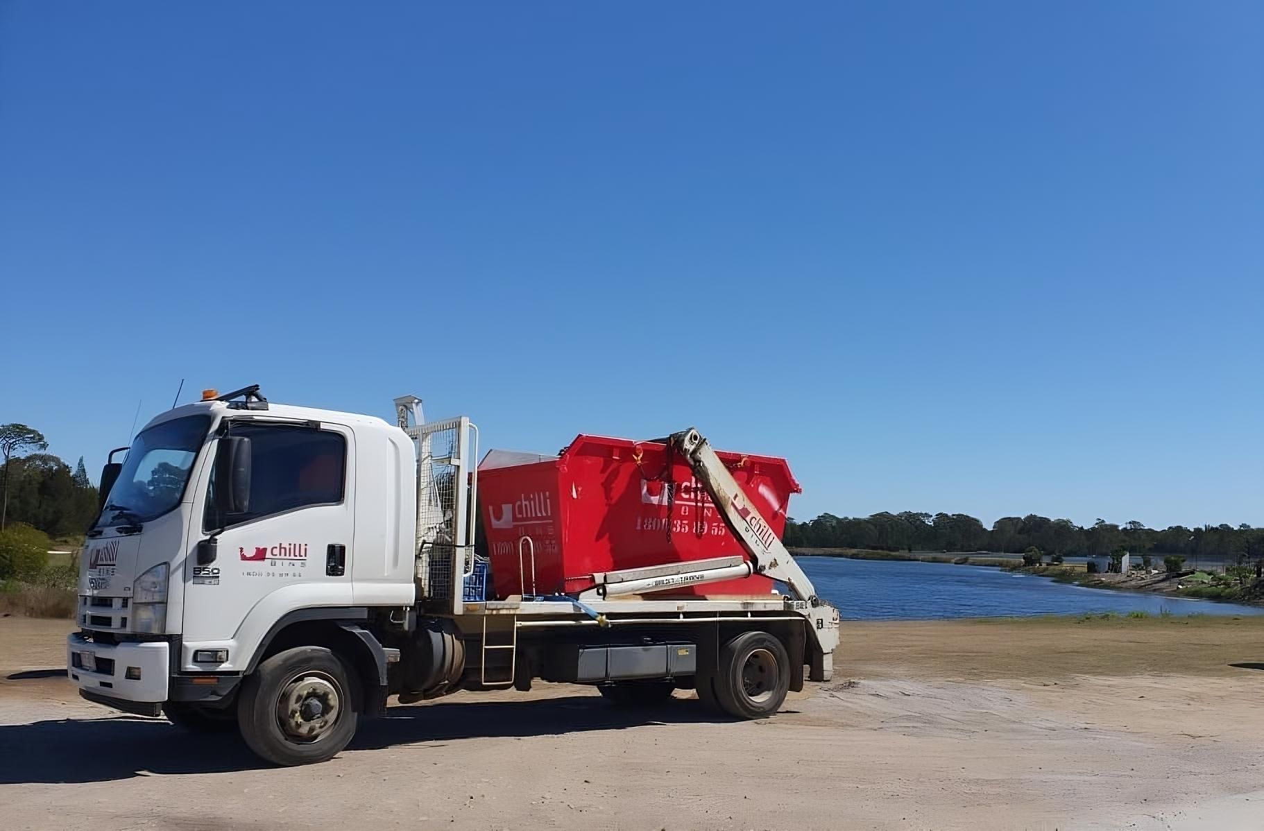 White Chilli Bins skip bin truck with red skip bin loaded, parked near waterfront in Australia