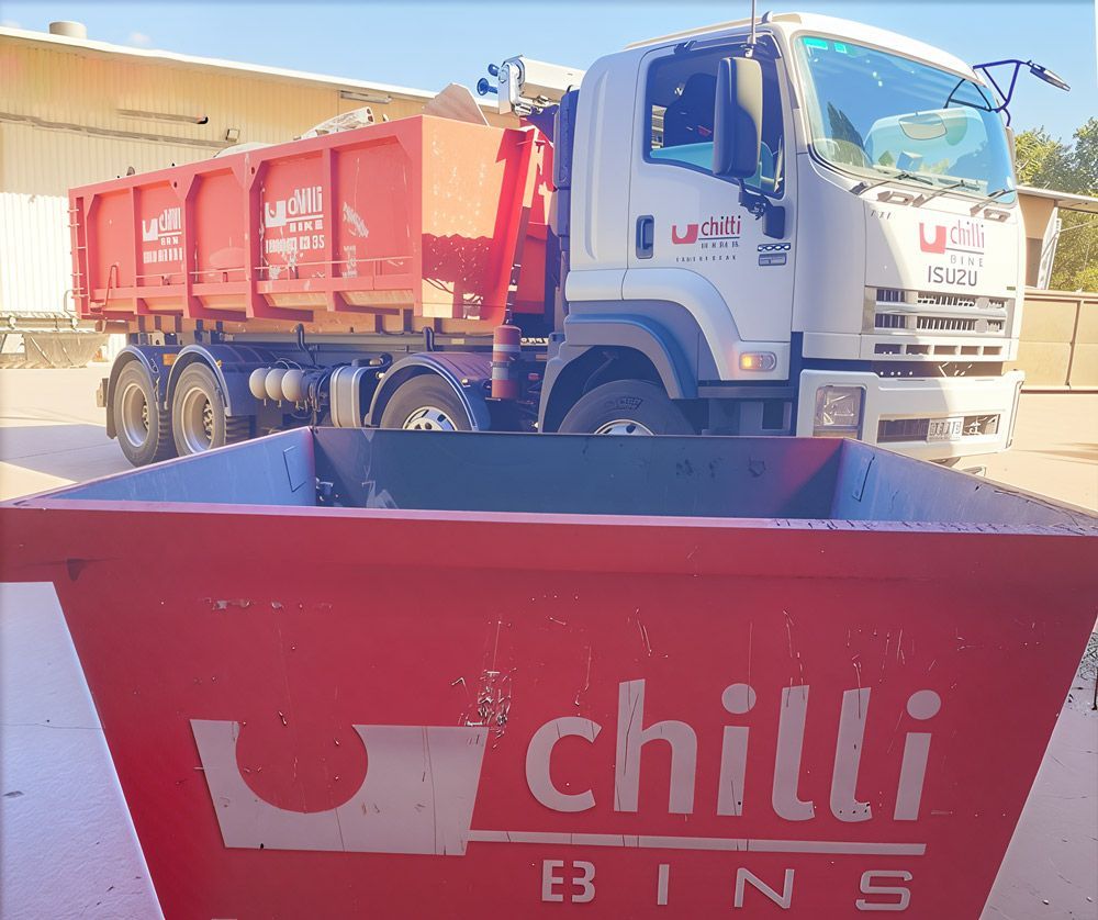 A skip bin in the foreground and a truck behind it.