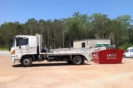 A White Dump Truck Is Parked Next to A Red Dumpster in A Dirt Lot — Chilli Bins Skip Bins in Glenview, QLD