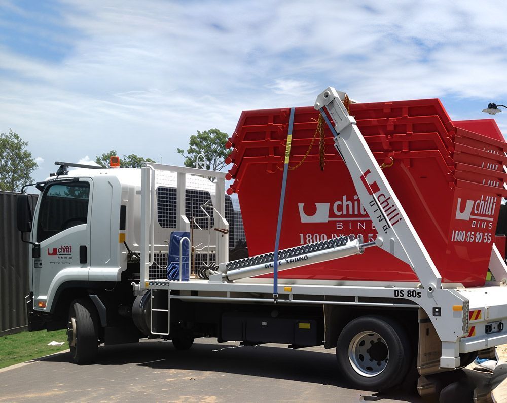 White Flatbed Truck Carrying A Large Red Dumpster — Chilli Bins Skip Bins in Redcliffe, QLD