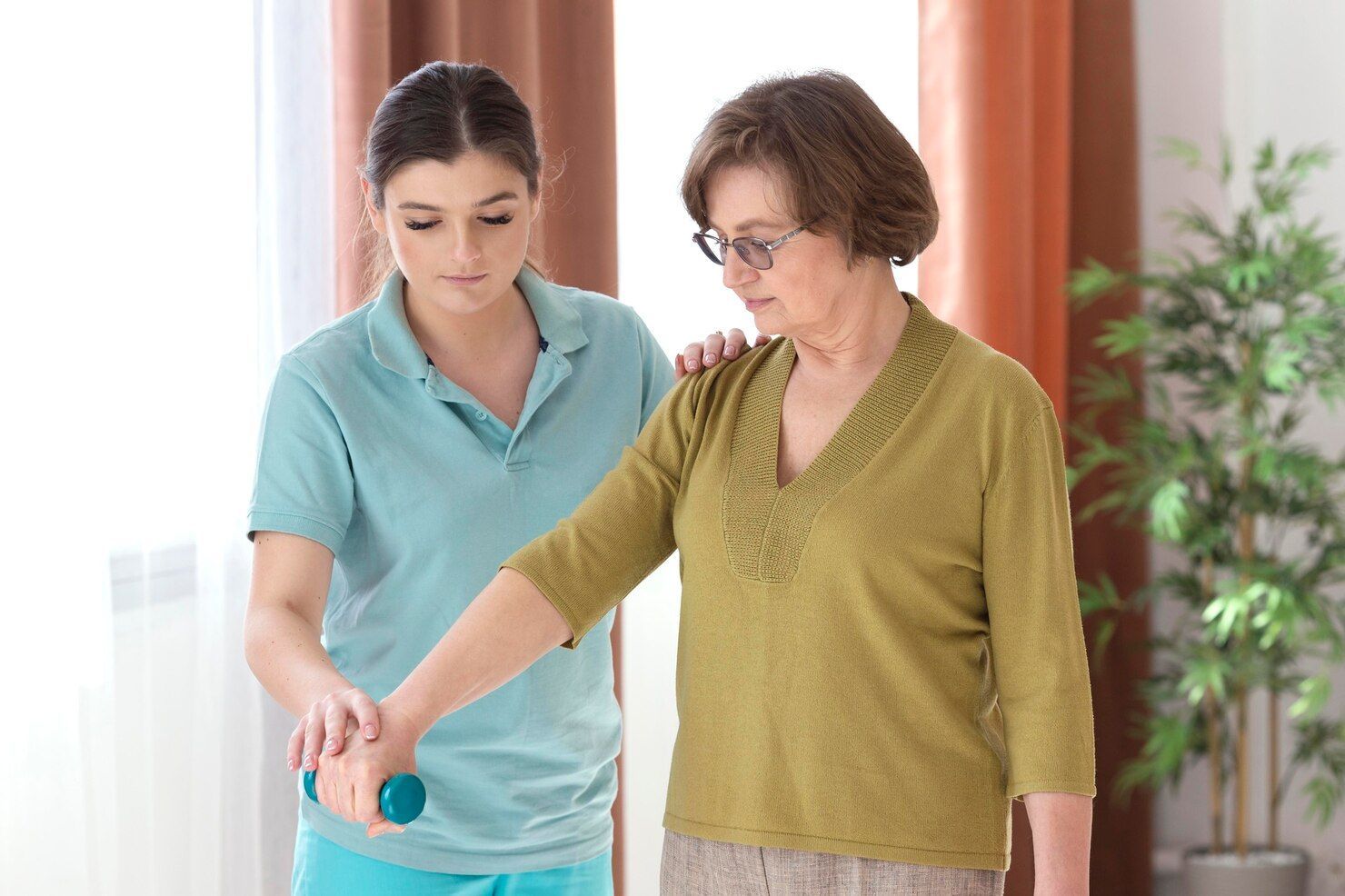 Caregiver assisting an elderly person with arm exercises using a small dumbbell.