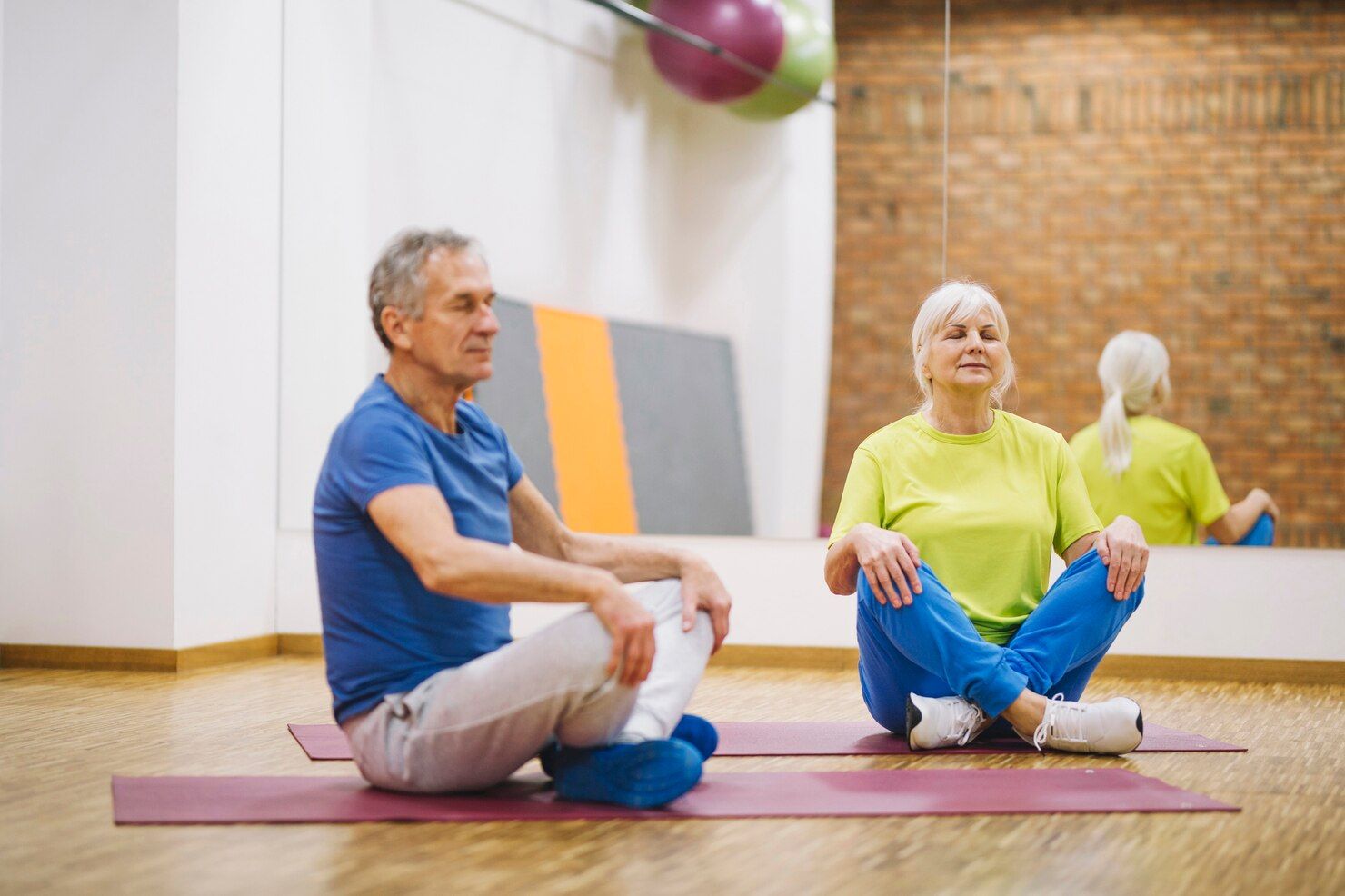 Two people seated on mats, indoors, meditating with eyes closed.
