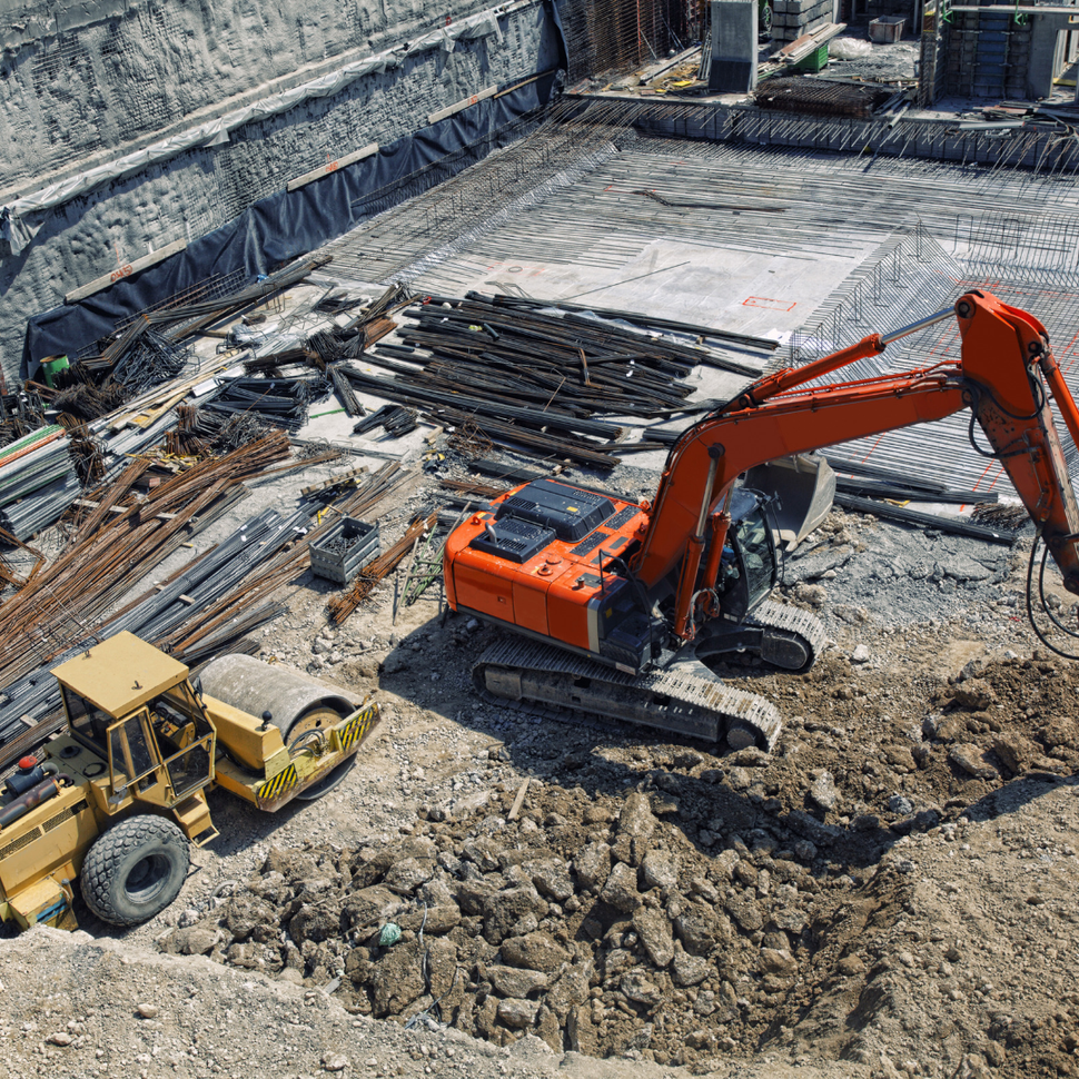 Orange excavator and yellow bulldozer working at a construction site with steel rebar and dirt piles