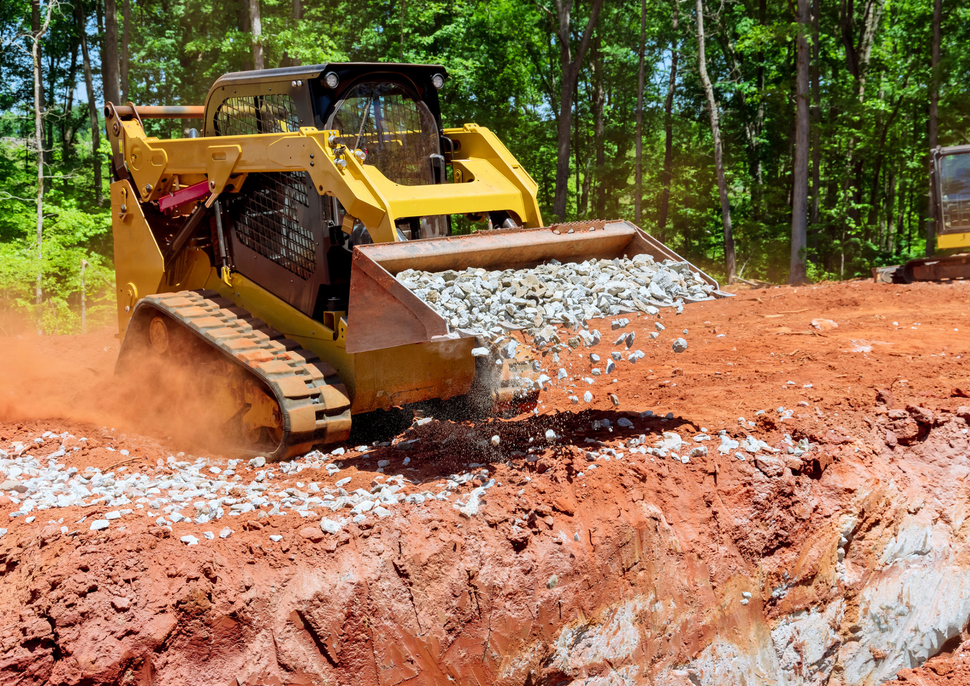 Yellow bulldozer pushing dirt and white rocks on a muddy construction site in a wooded area