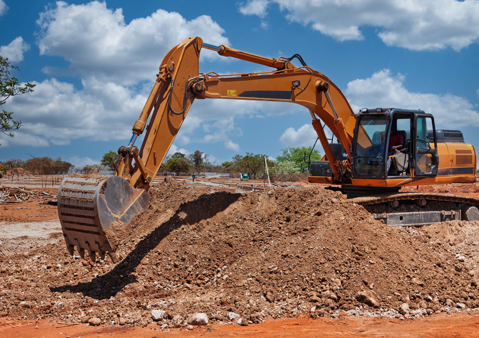 Yellow excavator digging a dirt mound under a blue sky on a construction site