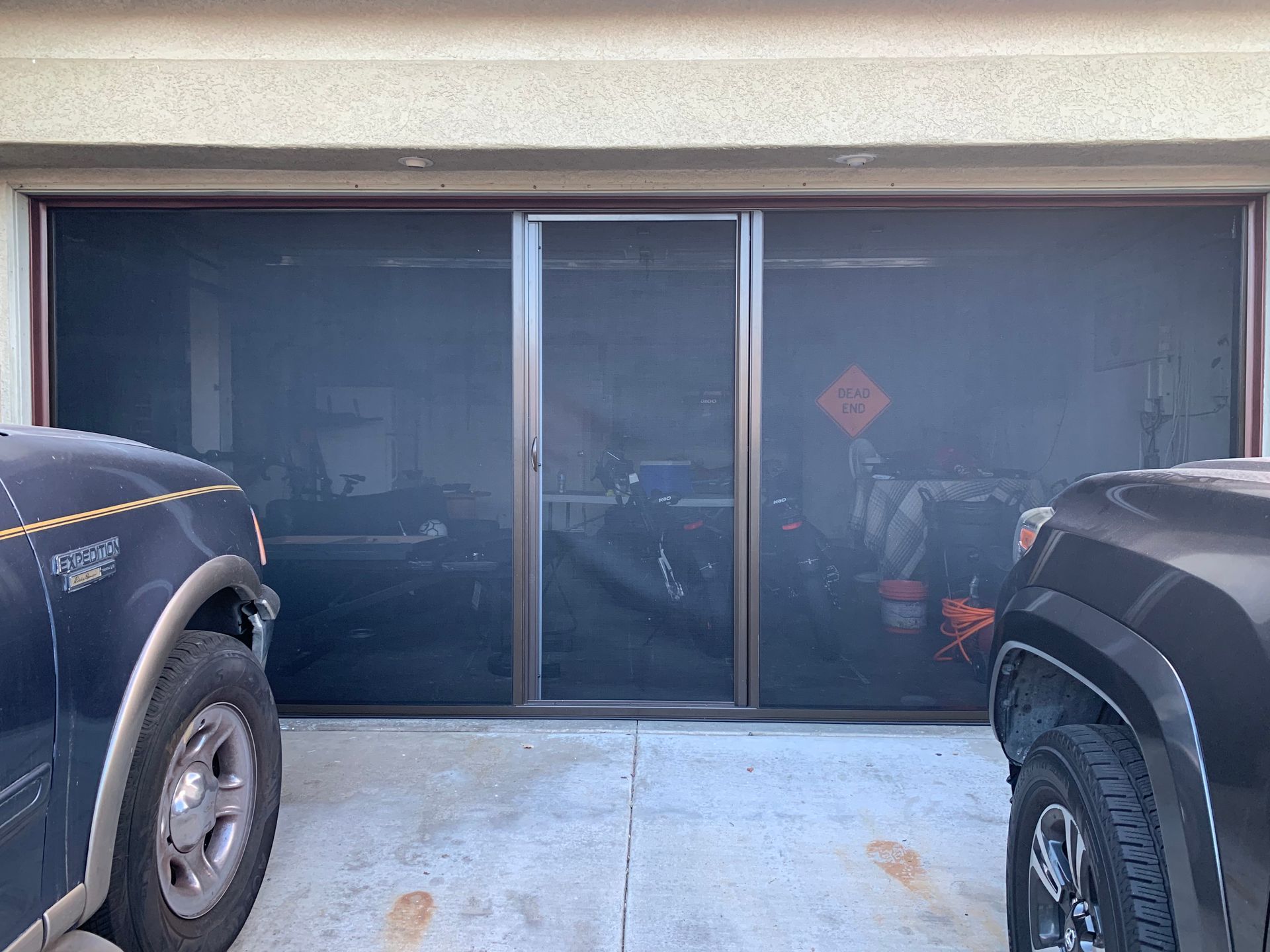 Two cars are parked in front of a screened in garage door.