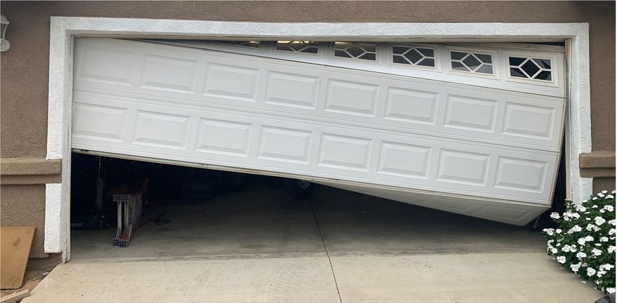 A broken garage door is sitting on the ground in front of a house.