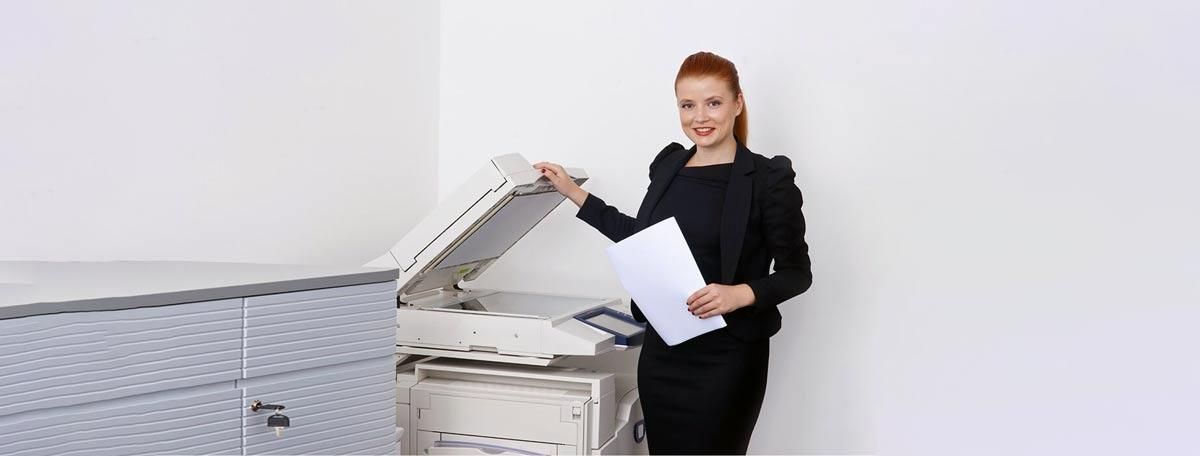 Una mujer está parada frente a una impresora sosteniendo un trozo de papel.
