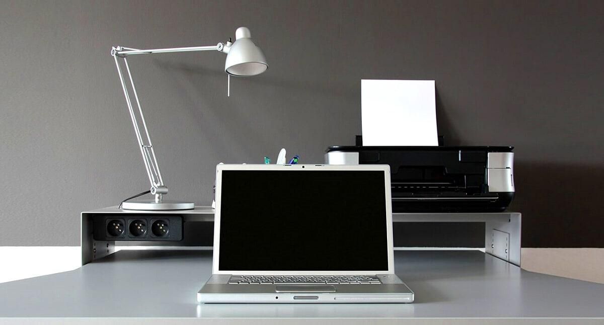 Una computadora portátil está sentada en un escritorio al lado de una lámpara y una impresora