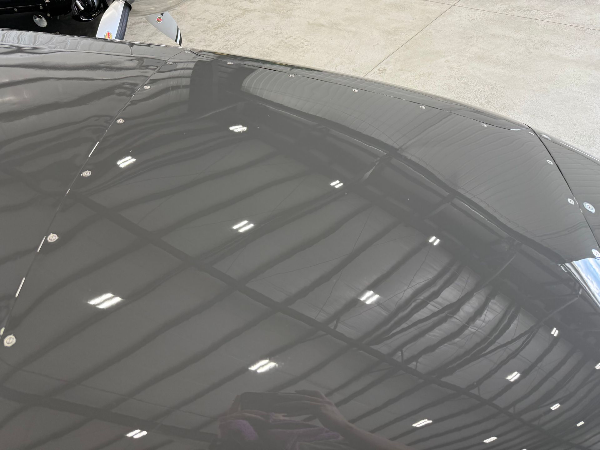 Shiny gray aircraft wing reflecting a hangar interior with lights and roof structure.