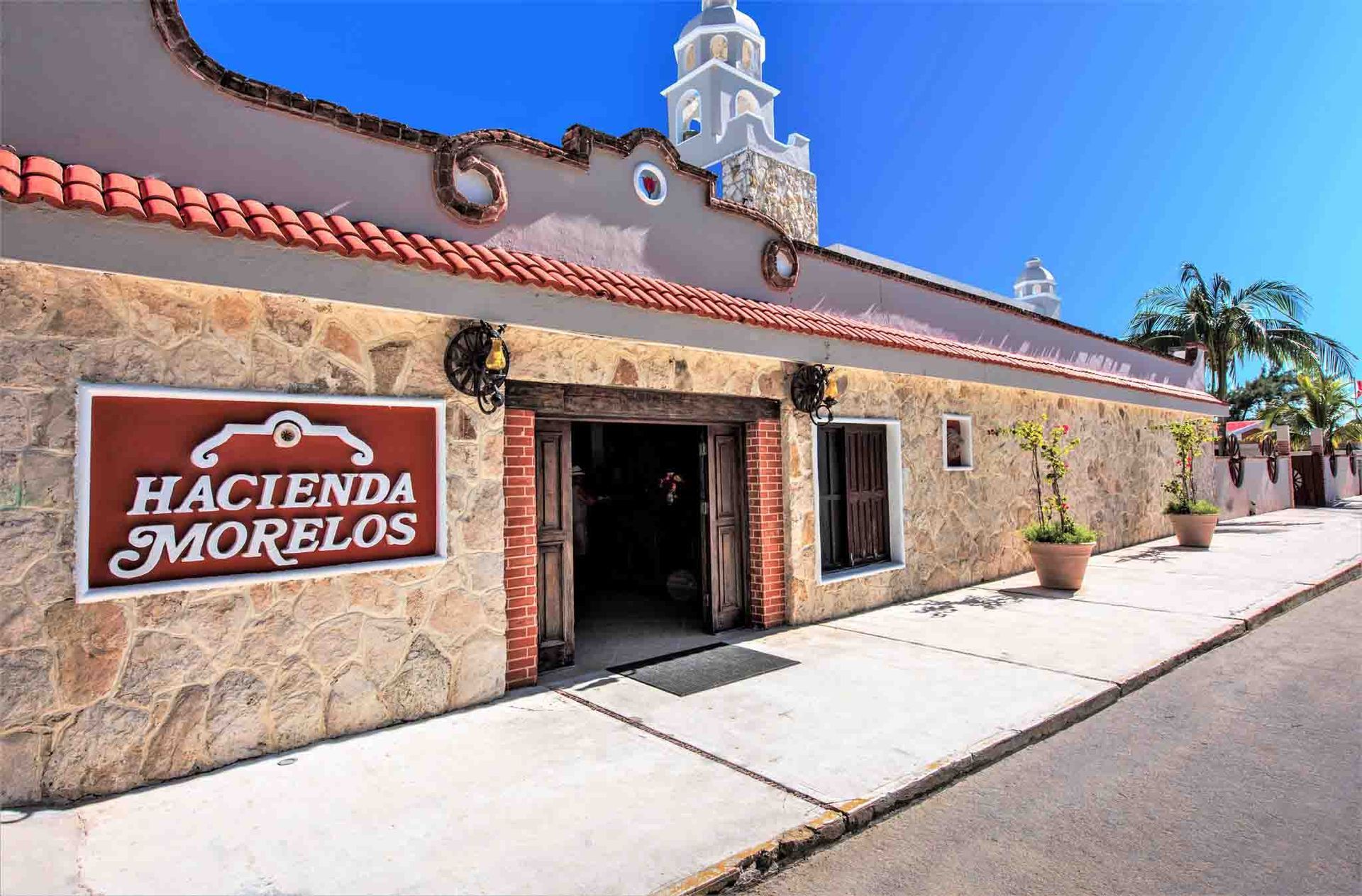 Hacienda Morelos restaurant exterior with stone facade, red sign, open door, and white tower.